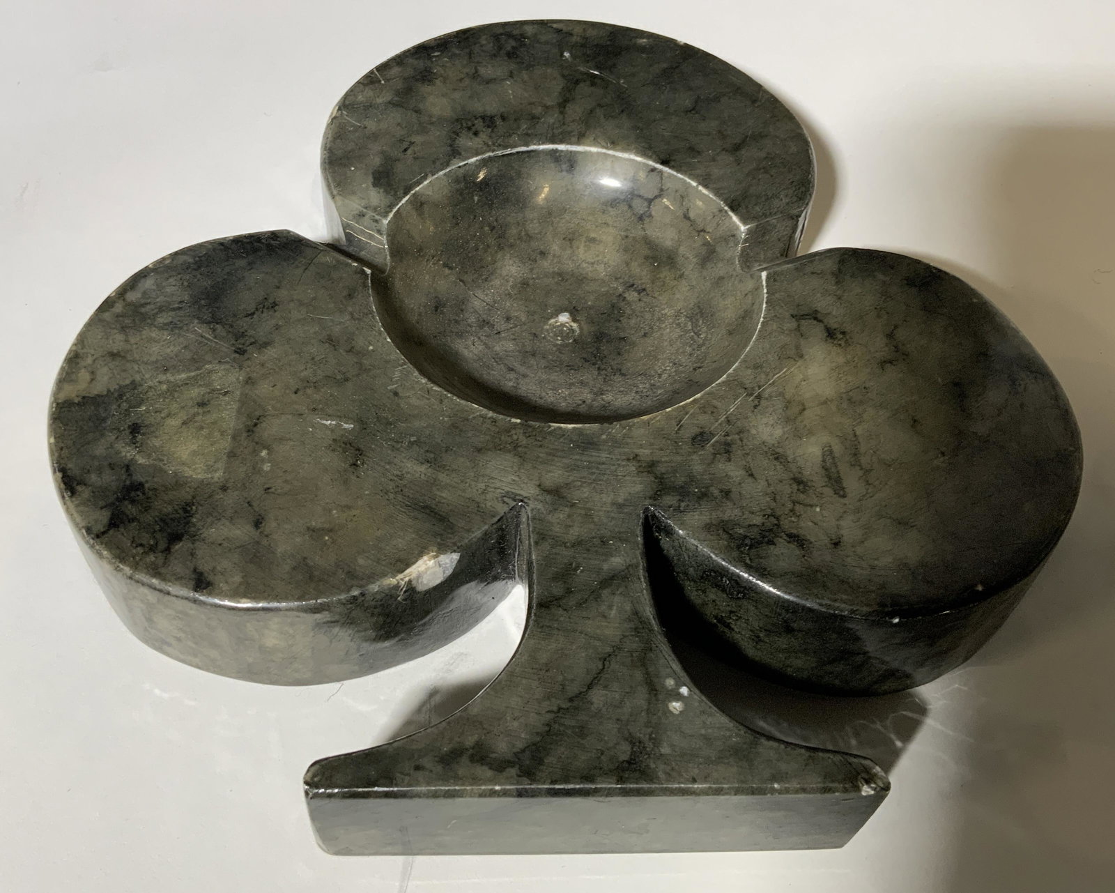 Stone Spade Shaped Ash Tray: Stone spade shaped ash tray, residue of label to reverse faded from age, made of a heavyweight Stone in a grey green color, chips and surface wear to piece, ash tray has two divots for cigarettes, mea
