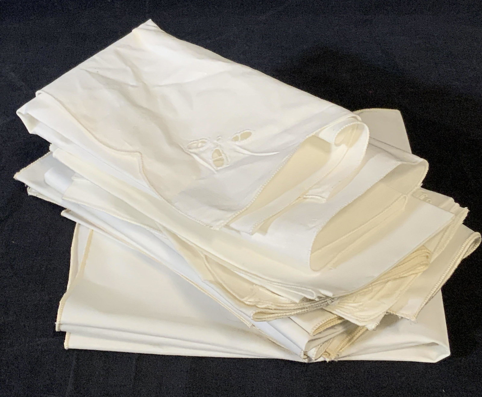 Lot 17 White Linen Table Napkins: Seventeen white linen table napkins. Possibly a linen blend. Pieces are white hued. Some have pierced fabric accents. Discoloration on some pieces. Approx. 16 x 16 inches unfolded. Piece are possibly 