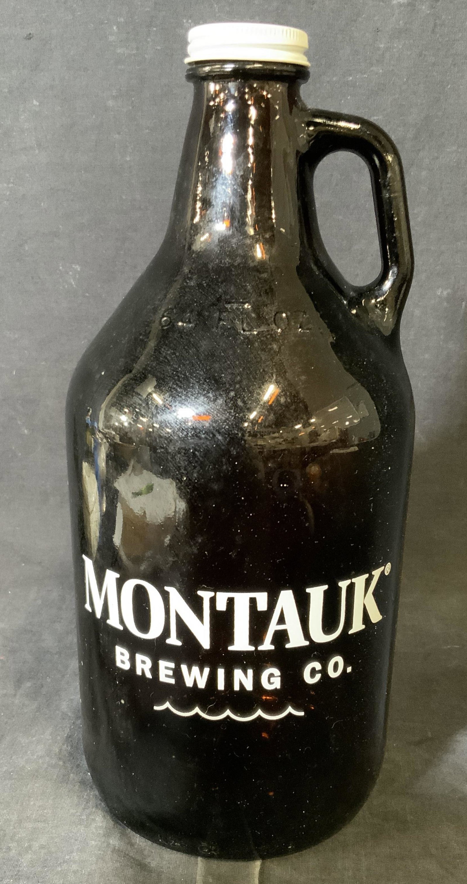 Montauk Brewing Co. Jug: Montauk brewing co. Jug, jug is made of a brown glass with white lettering to it, has a white painted metal lid, measures approximately 11.5 inches at tallest point, history of brewing company to reve