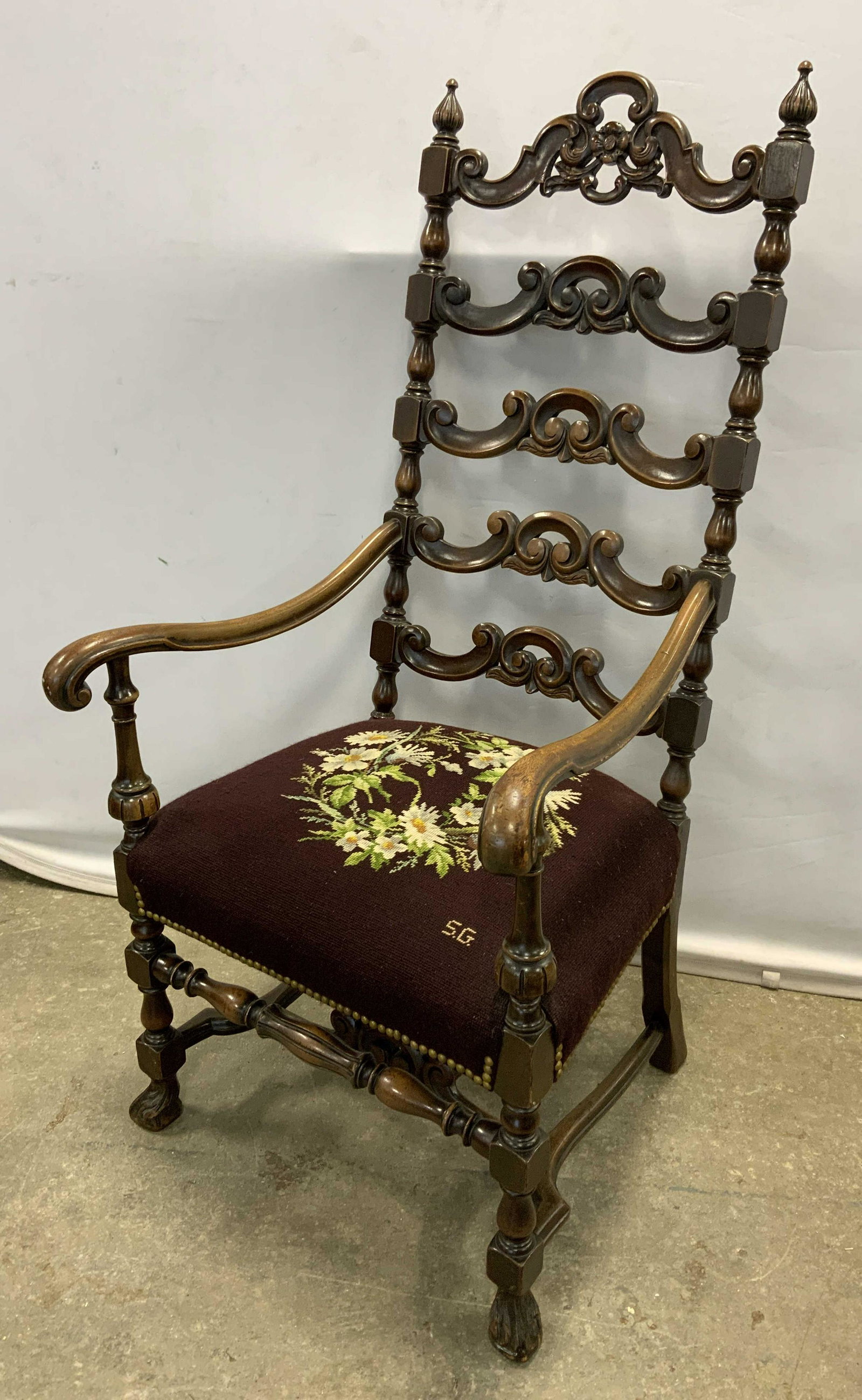 Vintage Ladder-Back Chair w Needlepoint Seat: Vintage, possibly antique, ladder back arm chair. Seat is upholstered, needlepoint design, depicts a floral wreath, initialed S.G. Upholstery secured with brass nails. Ladder back decorated with carve