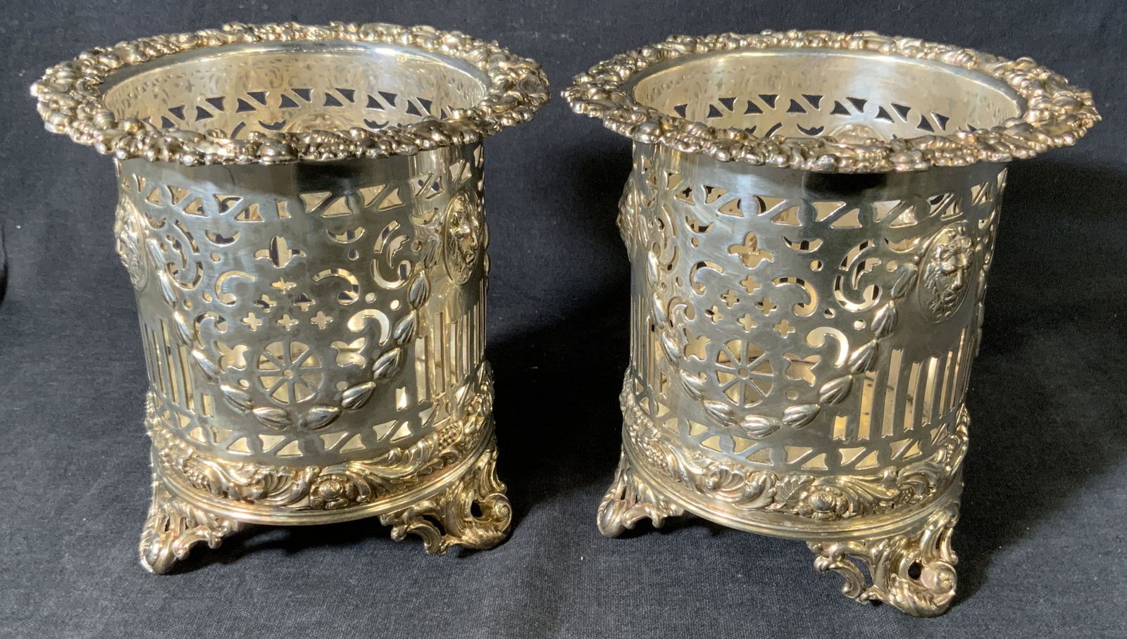 Pair Pierced Metal Wine Coasters: Pair Pierced Metal Wine Coasters, inscriptions to base read ‘SG’, features lion’s heads in medium relief, both measure 4 7/8 inches tall x 5 inches in diameter, surface wear and tarnishing to pi