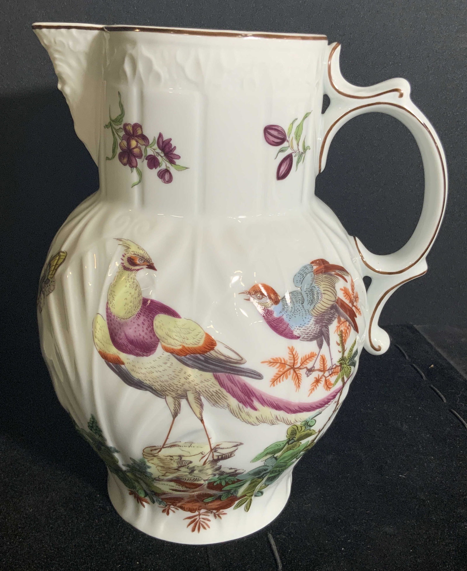 MOTTAHEDEH Williamsburg Porcelain Bird Pitcher: A white porcelain pitcher featuring colorful bird, insect, and floral designs. The piece has raised and impressed porcelain accents throughout. Spout of picture is crafted to resemble a man’s face. 