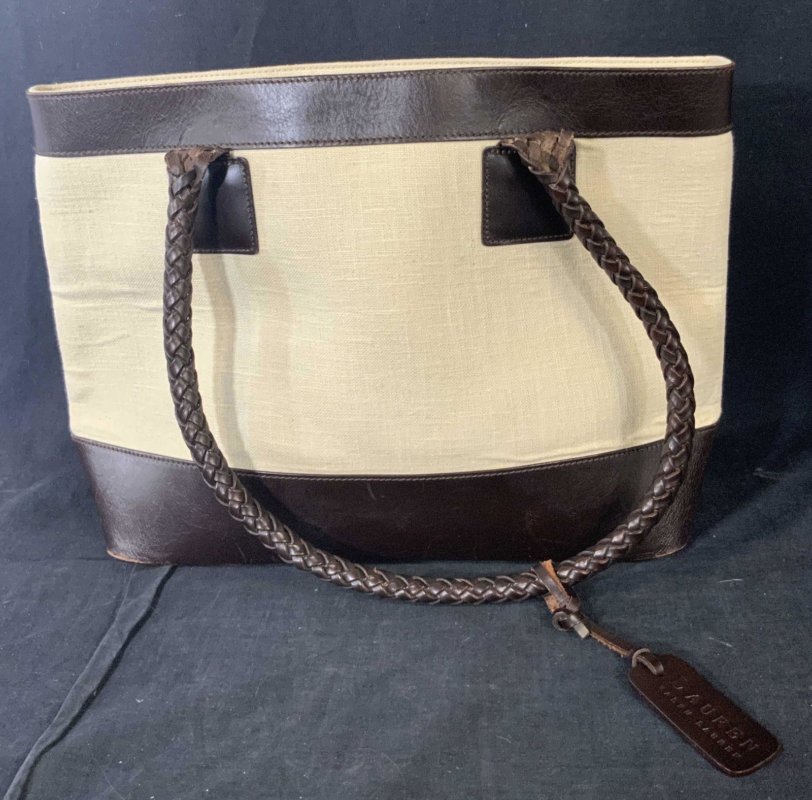 RALPH LAUREN Canvas & Leather Style Purse: A beige hued canvas style purse with deep chocolate brown leather style accents. Twin braided top handles. Charm affixed to handles reads, Lauren Ralph Lauren. Interior reads Ralph Lauren as well. Int