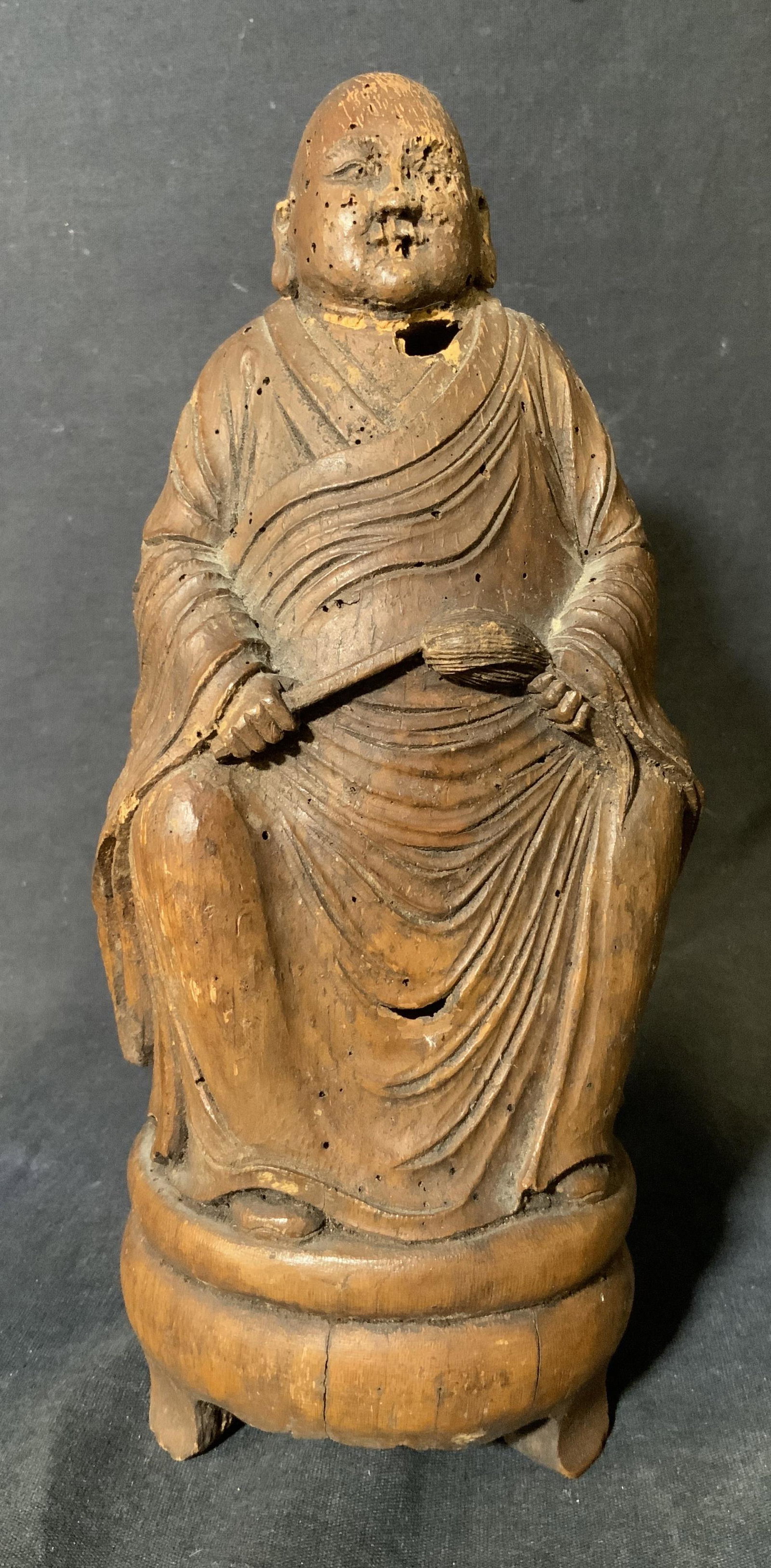 Wooden Buddhist Sculpture: Wooden Buddhist Sculpture, no apparent inscriptions or marks, a man in robes holding a brush, measures 9 1/2 inches tall x 3 3/4 inches wide at base, surface wear, losses, and insect tunneling to wood