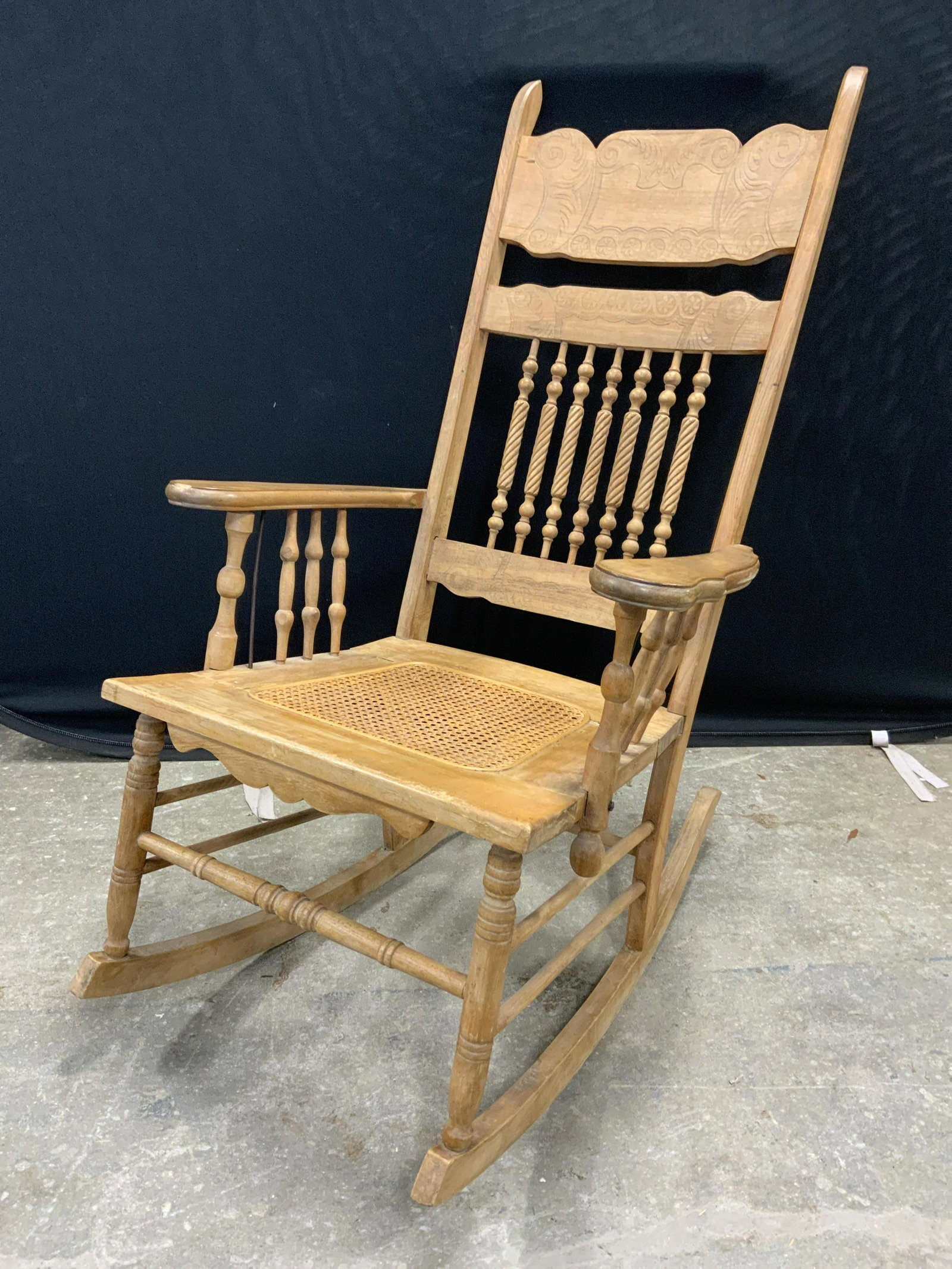 Vintage Wooden Rocking Chair: Vintage, possibly antique, wooden rocking chair. Seat appears to be cane, back decorated with feather like detailing. Wear is consistent with age and use, evident surface wear, loosening of joints. Me