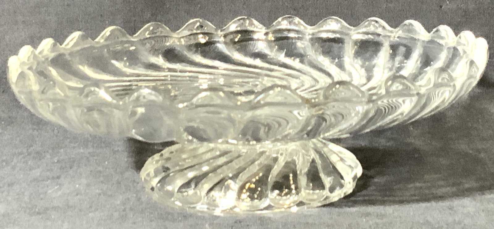 BACCARAT Signed French Crystal Pedestal Dish: A swirled crystal pedestal dish. Piece has blunted saw tooth edge design. Seems are visible. Underside signed Baccarat. Measures approx. 2.5H x 7W in. Some chipping to piece, surface wear consistent w