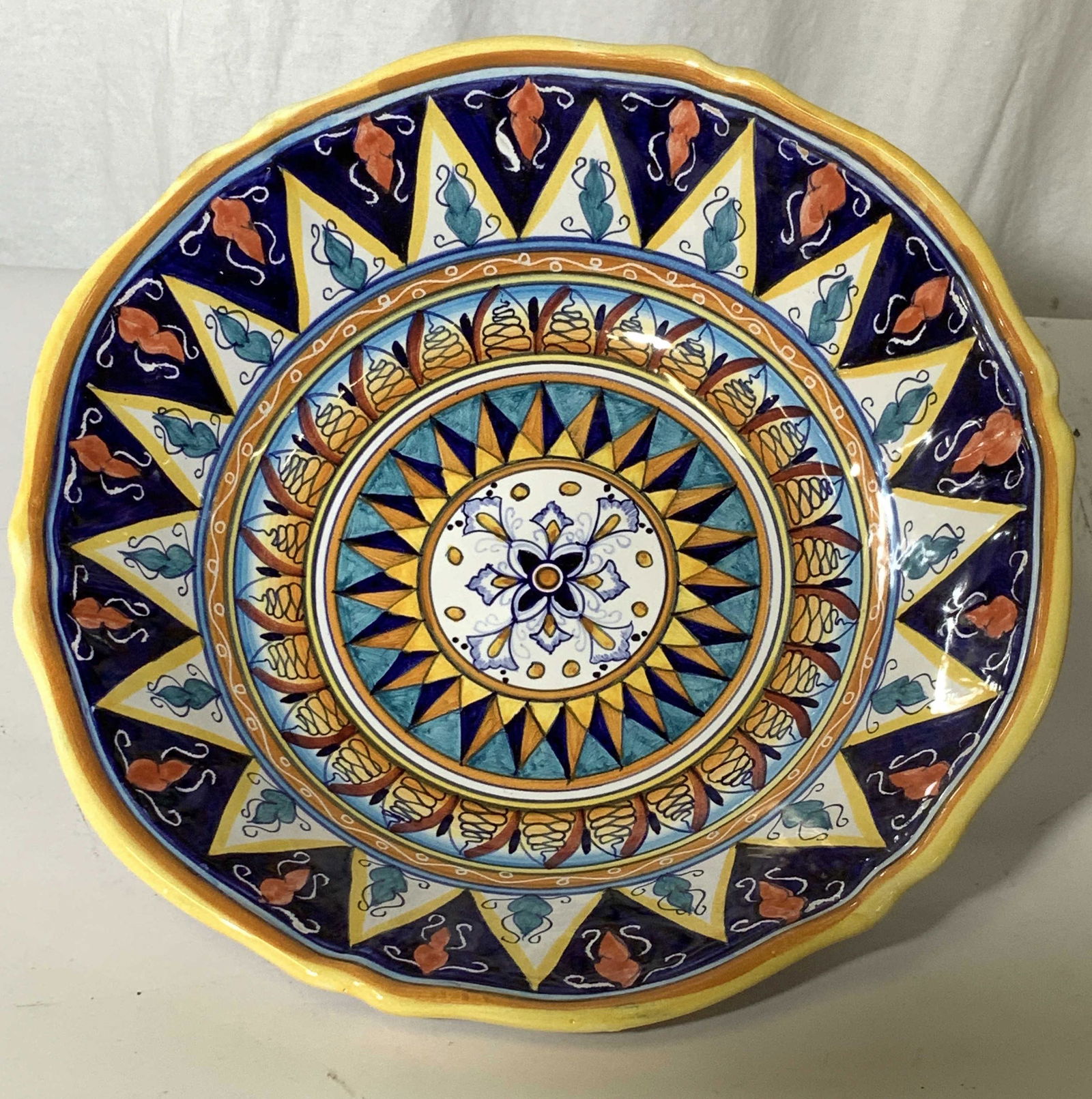 Hand Painted Glazed Artisanal Pottery Bowl, Italy: Hand painted Round pottery, Made in Italy, multi geometric designs with center sunburst. intense yellow, cobalt blue, and coral color palatte. Hallmarked DIP A Mano Made in Italy. 12 in in diameter by