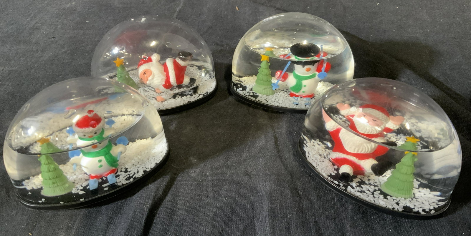 Set of 4 KCARE Christmas Snow Globes: Set of 4 KCARE Christmas Snow Globes, inscriptions to base of each reads ‘Kcare’, two depicts skiing snowmen and two depict Santa, all measure 2 3/4 tall x 3 3/4 inches at widest point, some liqui
