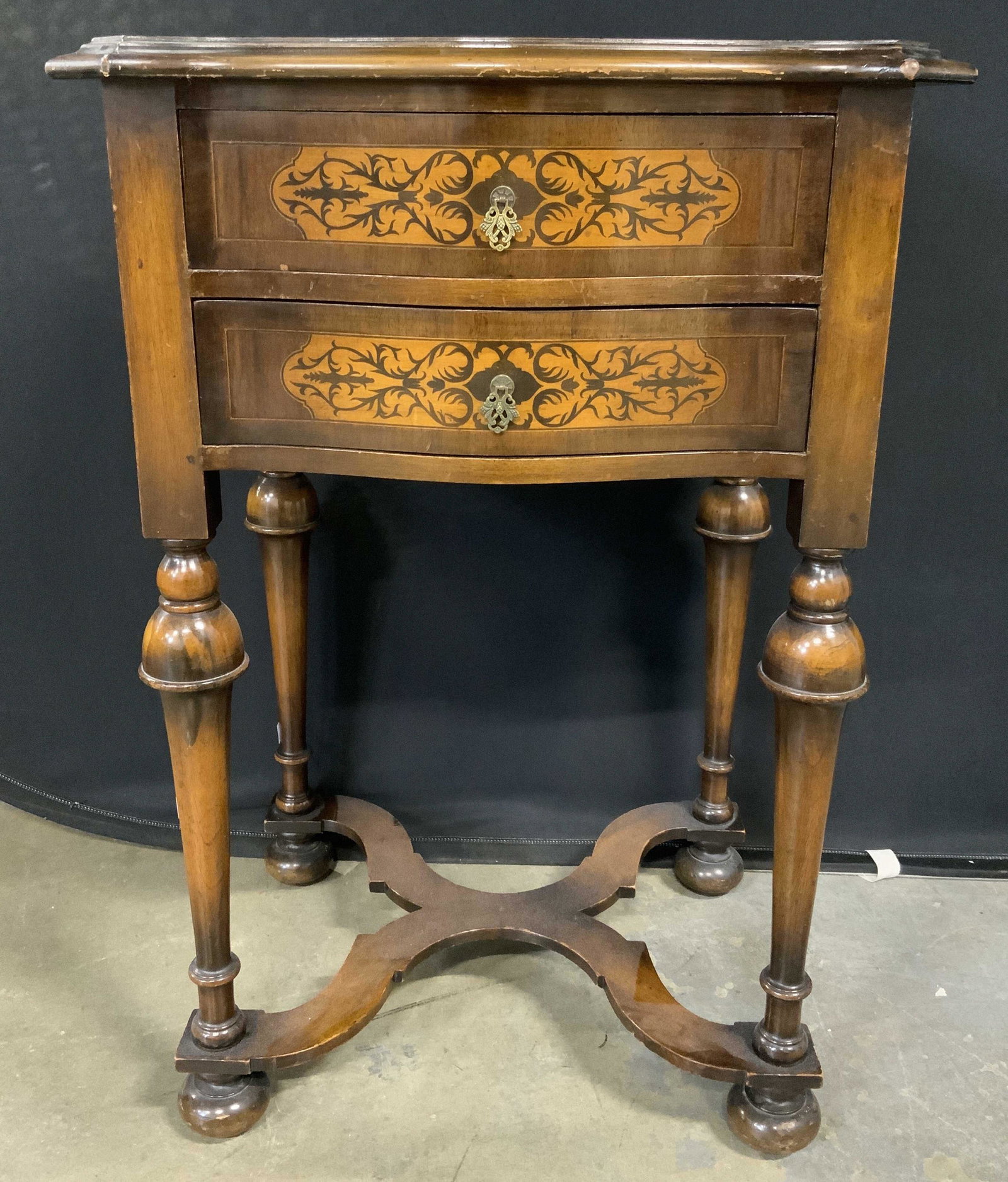 Antique Wooden Night Stand: Antique wooden night stand, possibly French. Four legs, taper downward, connected by an x-shaped stretcher, rests on four bun shaped feet. Top and drawers decorated with multi toned inlaid wooden deta