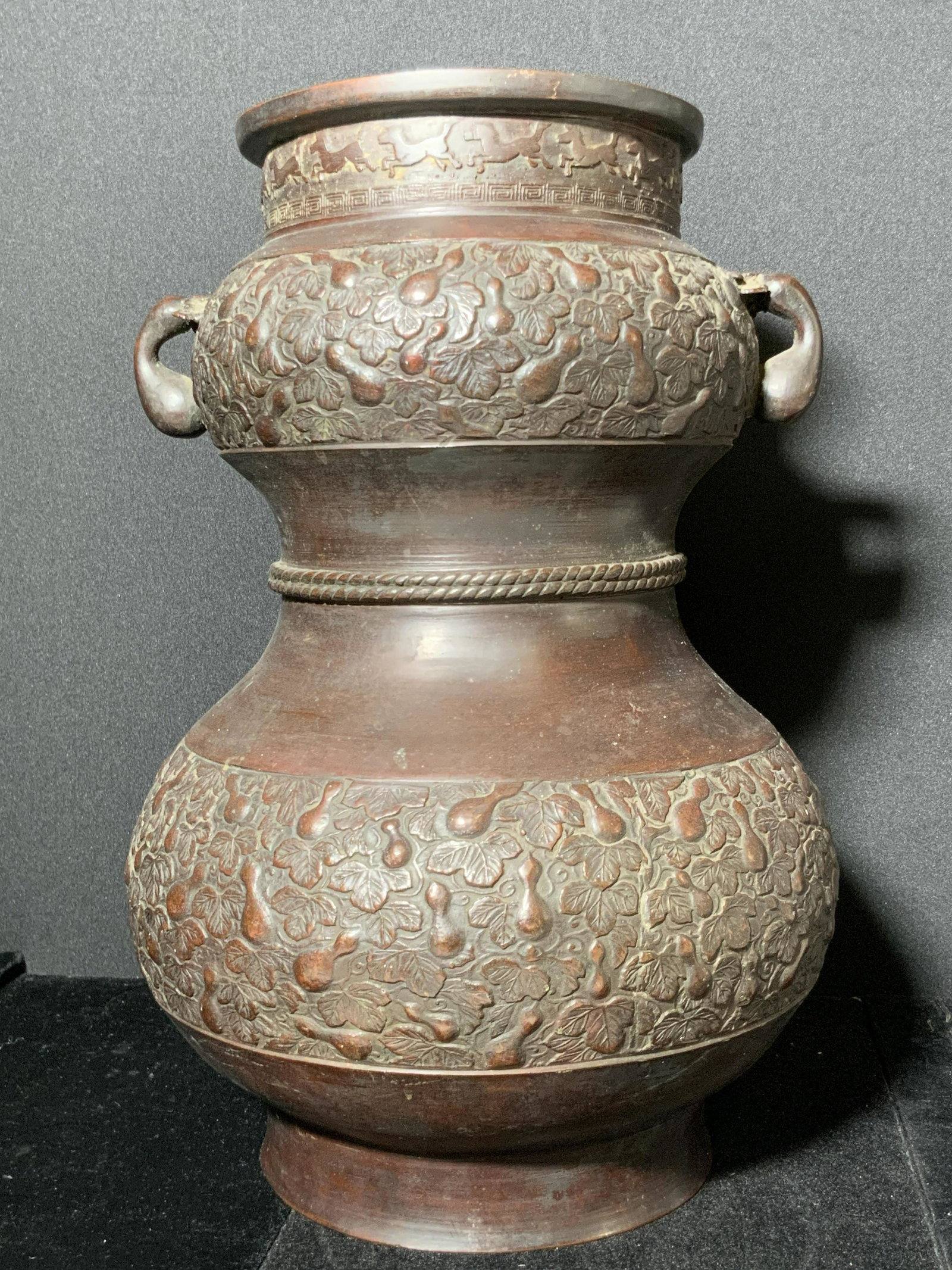 Vintage Signed Asian Gourd Motif Vase: A weighty metal gourd vase that has been painted a deep brown-red hue. Piece features raised gourd motifs and a raised braided bow on the center. Twin handles on either side. Raised horse and key moti