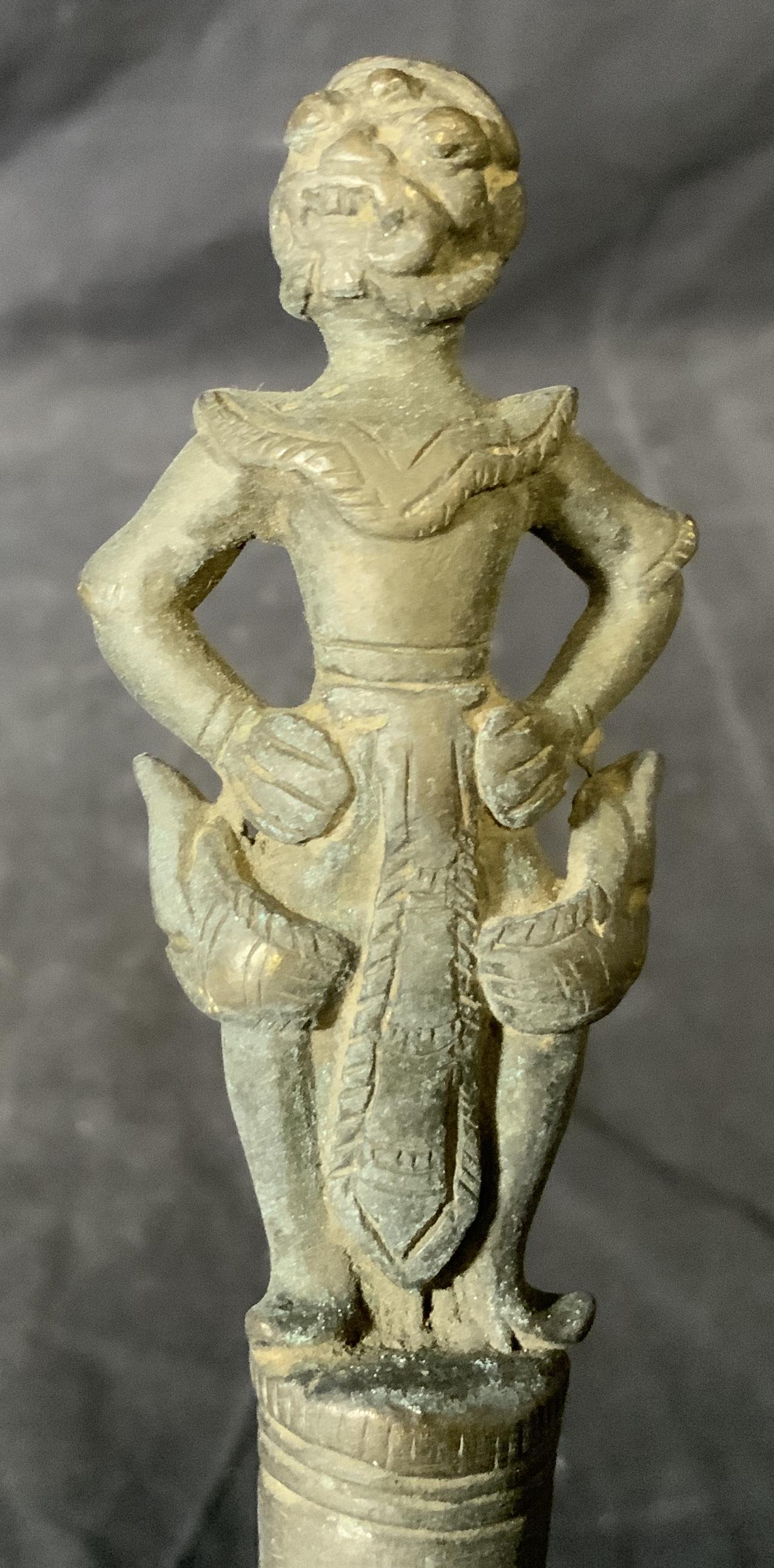 Indian Metal Ornament: Indian metal ornament, ornament is in a pole like shape with a hole at one end for placing it atop something, finial to top of piece depicts a human figure in traditional garb, piece measures 12 inche