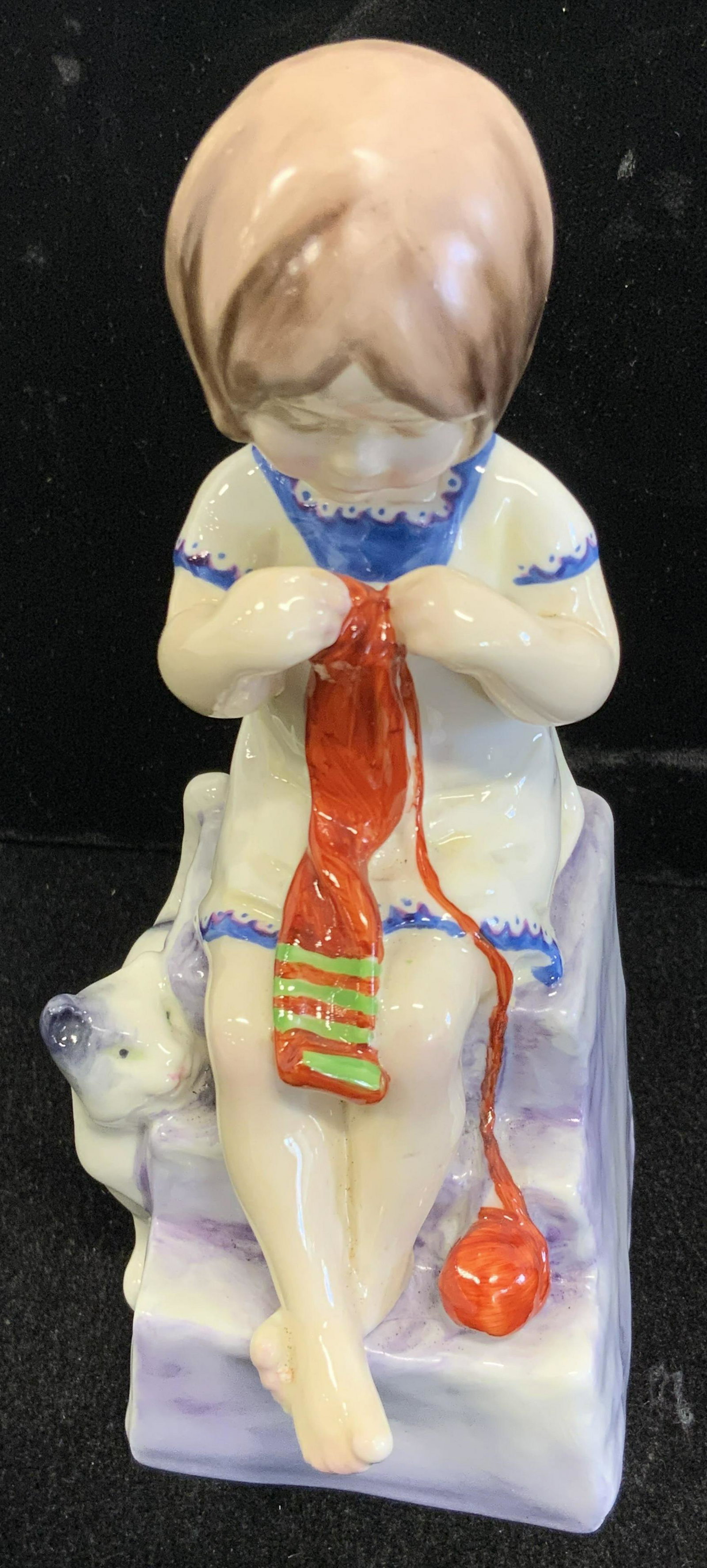 ROYAL WORCESTER Bone China Cat & Child Figural: A fine bone china hand painted figural depicting a young girl sitting upon the steps of her home knitting a scarf. Her cat stands beside her, eyeing the ball of yarn. The piece is primarily white, blu
