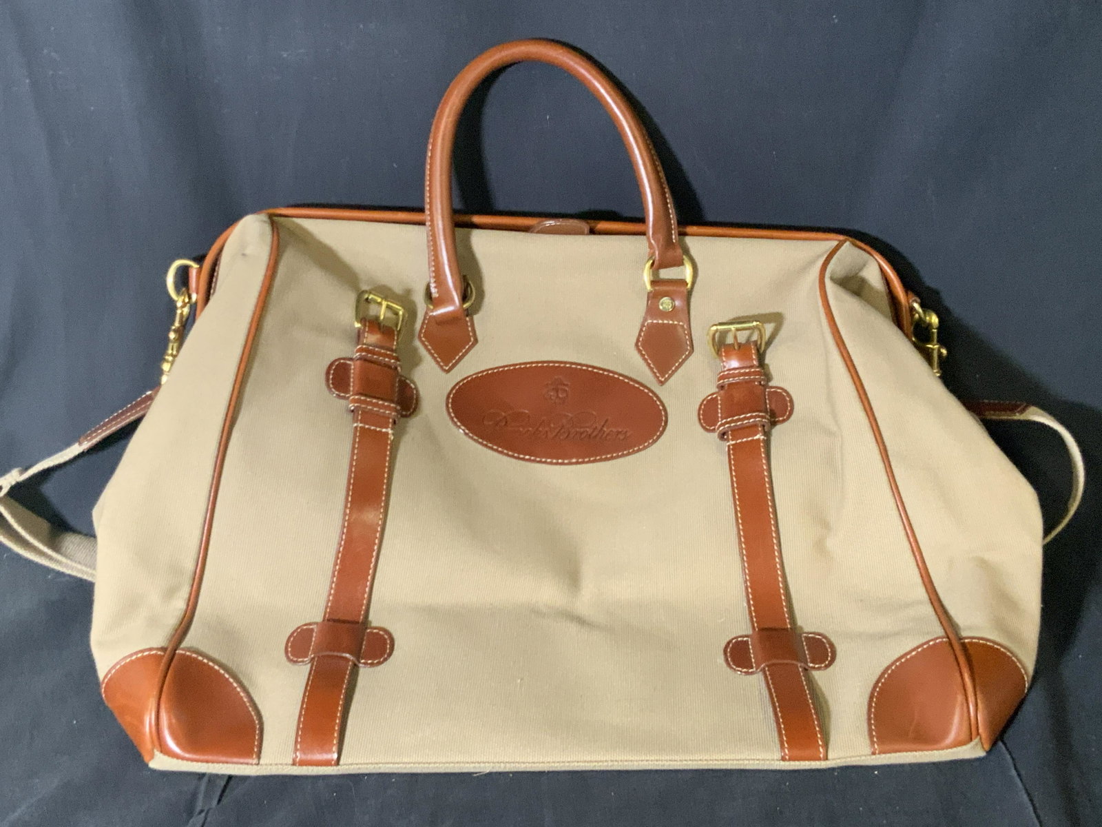 BROOKS BROTHERS Vintage Travel Bag: A oversized vintage Brooks Brother travel bag. Primarily beige and brown hued. Canvas and leather style material. Underside has gold hued metal feet. Gold hued metal hardware throughout. Shoulder stra