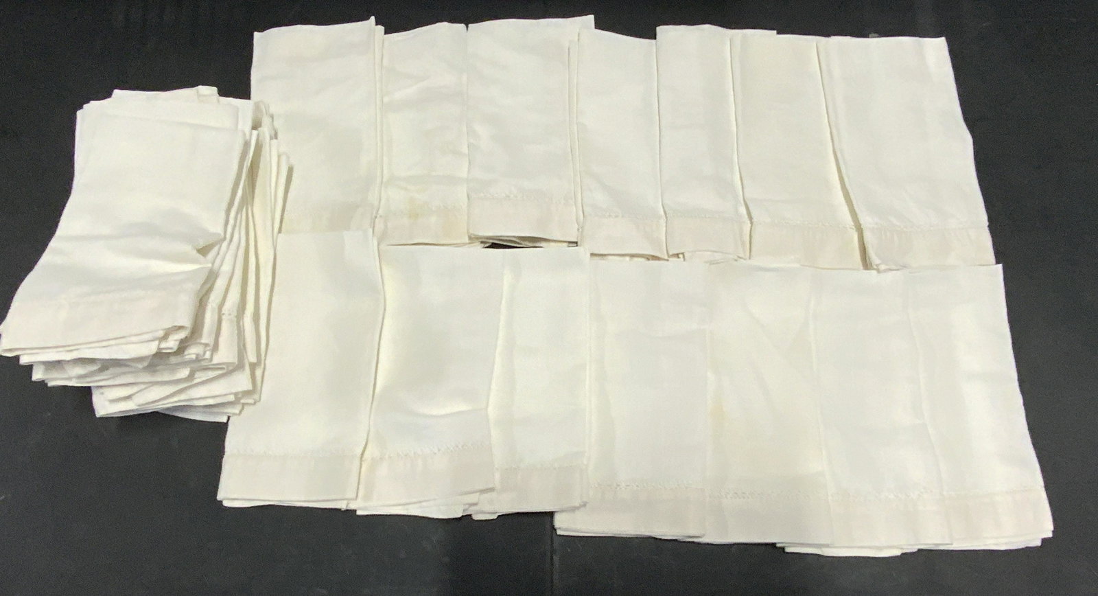 Lot 30 White Linen Tea Towels: Thirty white hued linen blend hand towels. The pieces are edged with off white accents and pierced fabric designs. Pieces have some discoloration. Approx. 22 x 22 in. Linens, tea towels, hand towels,