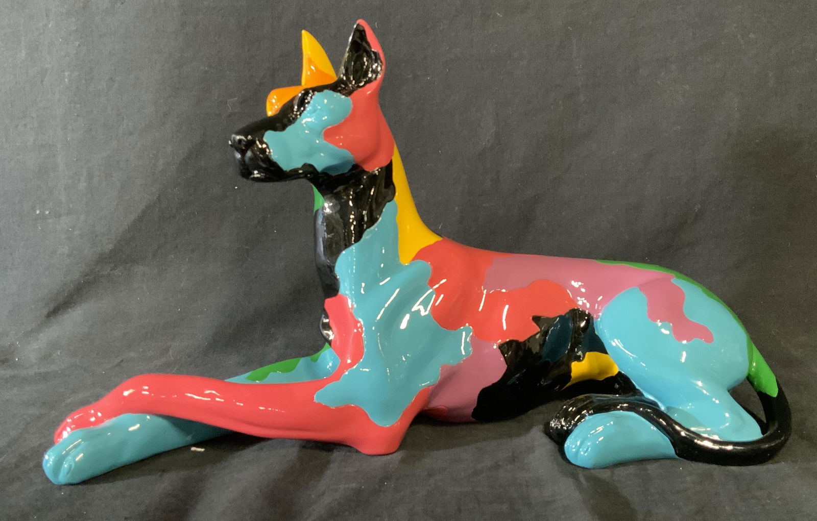 Colorful Doberman Sculpture: Colorful Doberman Sculpture, no apparent inscriptions or markings to piece, subject a Doberman sitting on all fours with front legs crossed painted in blotches of yellow, blue, pink, and purple, black