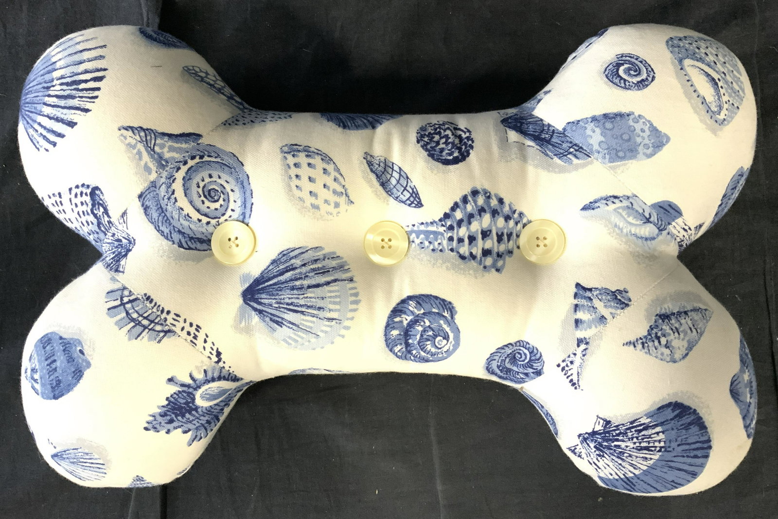Dog Bone Pillow W Shell Detail & Buttons: Pillow has shape of dog bone. Piece is cream toned with blue toned shell detail. Center of piece has 3 buttons in center. Piece measures approx 18 inches long 12 inches tall 4.5 inches deep. Bone pill