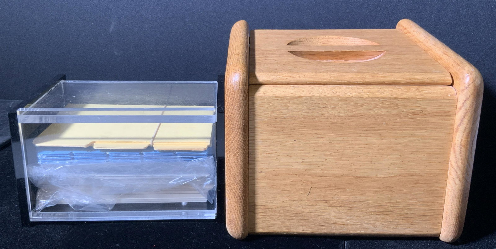 Lot 2 Lucite & Wood Storage Vessels: One clear and black lucite index card / storage vessel. Obverse opens. Interior possesses some paper product. Larger piece is crafted from wood. Top opens. Measures approx 6H x 6W in. Both pieces poss