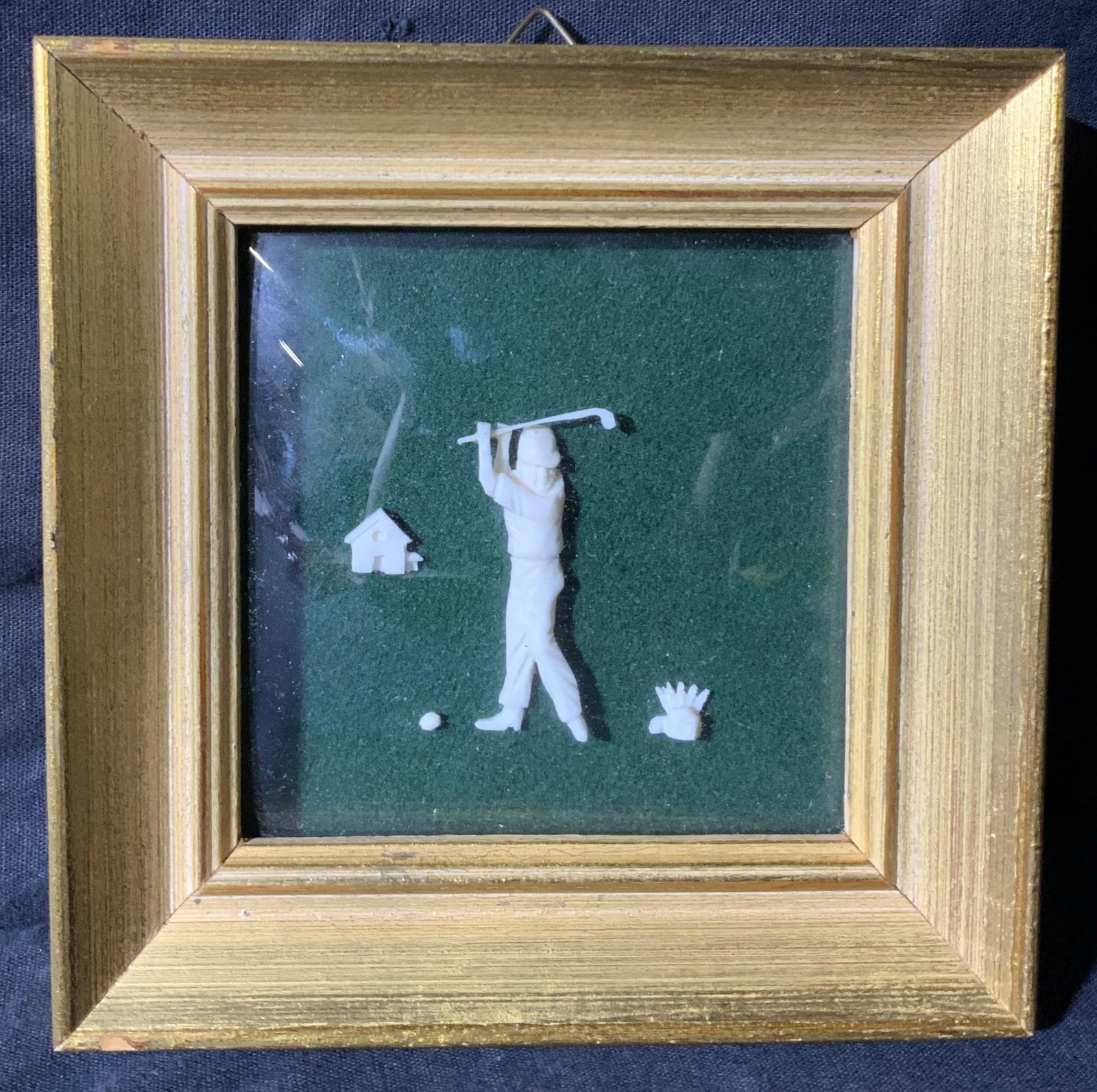 Framed Carved Bone Golfing Scene: Framed Carved Bone Golfing Scene, no apparent inscriptions or marks to piece, subject a man holding a raised golf club about to hit a golf ball, set against a green background, frame measures 5 1/8 x 