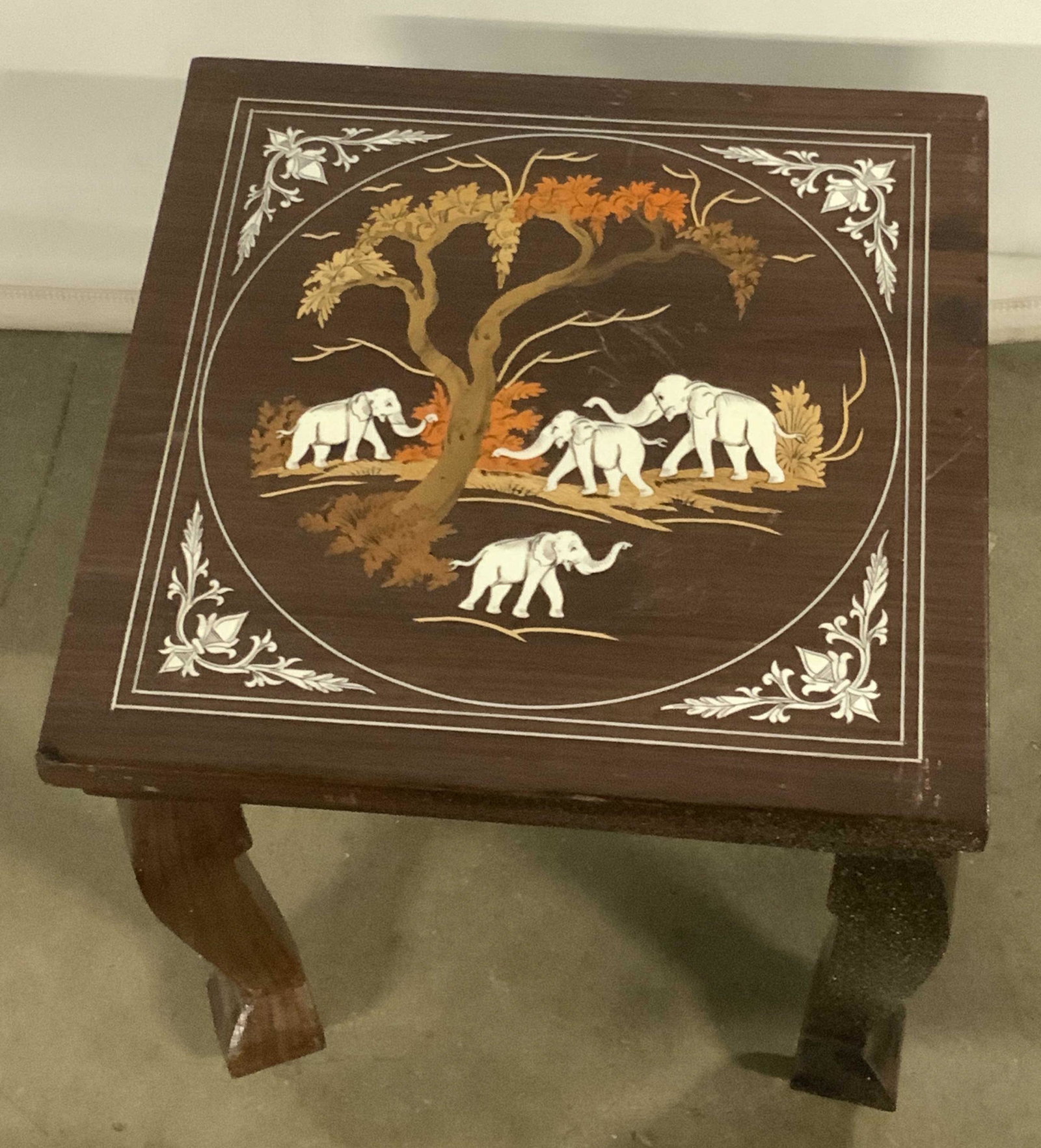 Vintage Inlaid Elephant Motif Wood Display Stand: A vintage wooden display stand decorated with inlaid elephant motifs. Piece is primarily a rich brown hue. Elephants are white hued, foliage is lighter brown and orange hues. Measures approx 12Height 