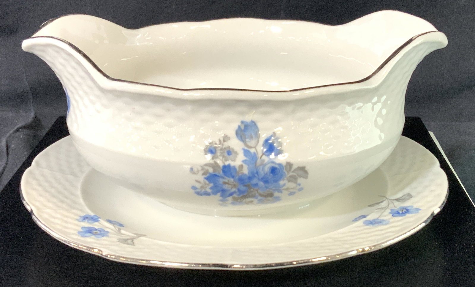 Fine Bone China Gravy Boat, Czechoslovakia: Vintage porcelain gravy boat with dual sided pouring spout. Hand painted with blue tulips and roses, embossed basket weave pattern. Bowl is connected to drip plate. 6.5 x 5 x 3 in. Hallmarked on verso