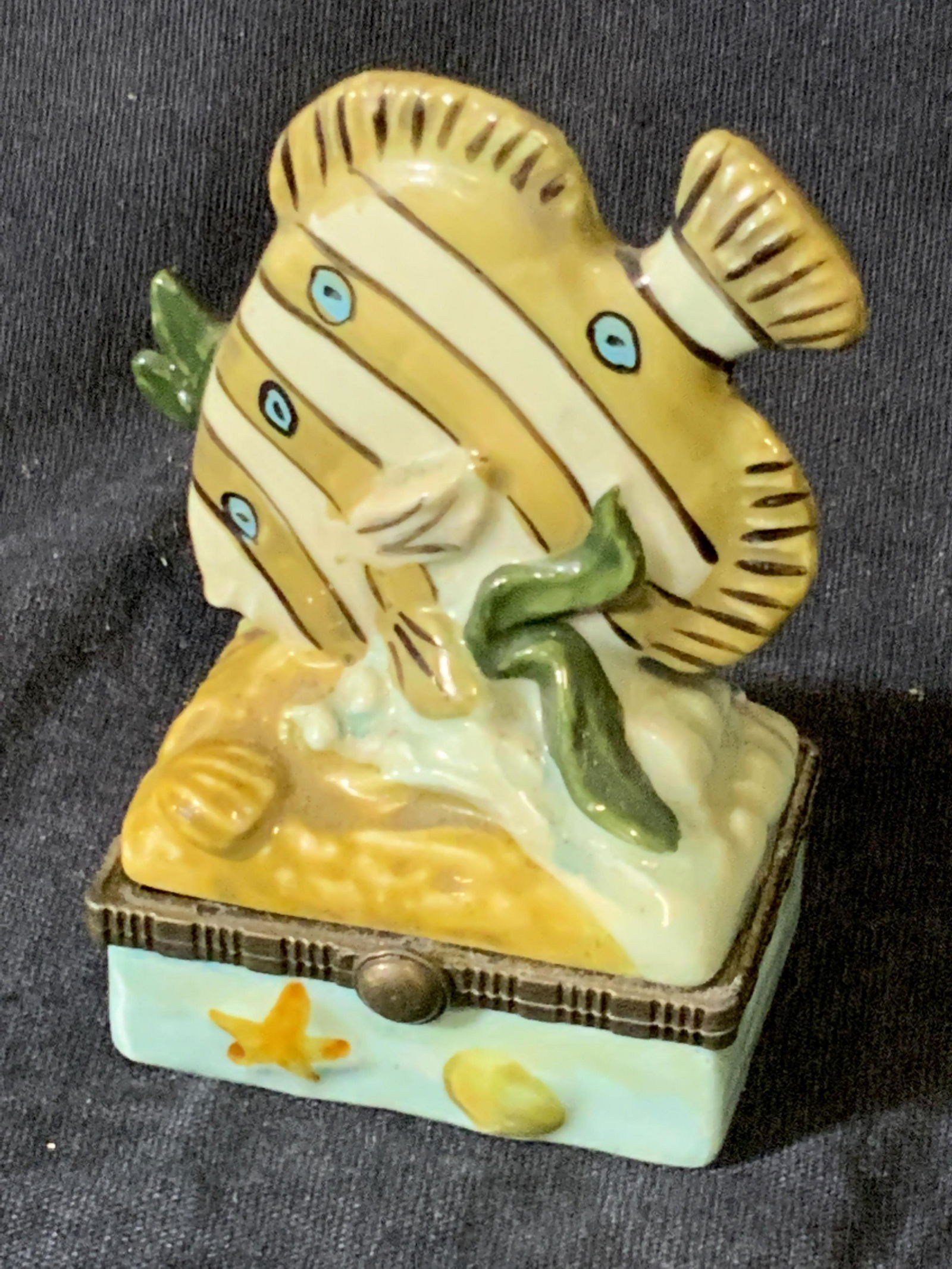 Fish Form Porcelain Pill / Trinket Box: A porcelain trinket/ pill box crafted into the form of a fish. Painted elements throughout. Marine motifs throughout. Box opens with metal hinge hardware. Measures approx. 3H x 2W in. Some wear consis