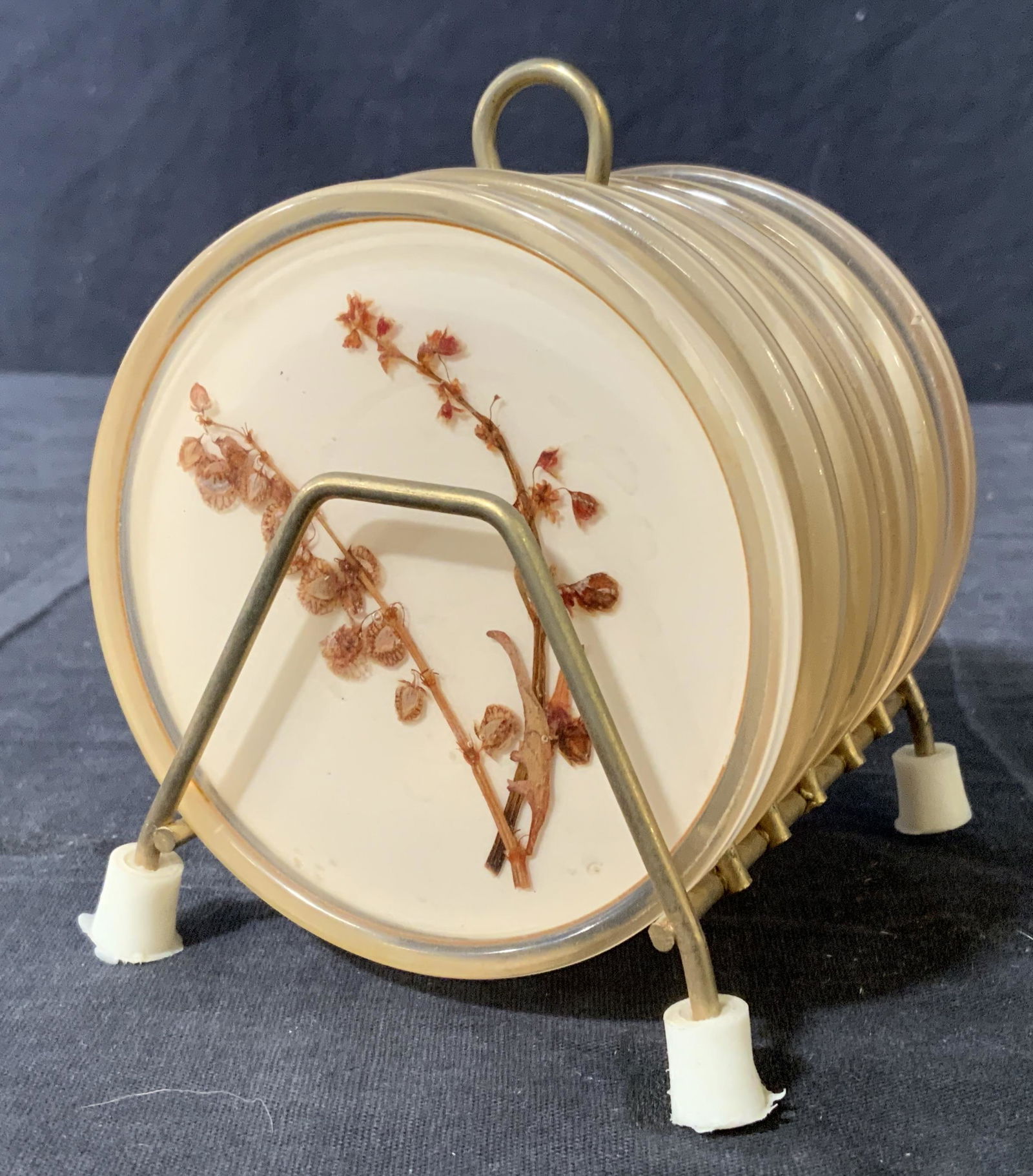 Set 6 Dried Flower Coasters, Israel: Set 6 coasters. Underside of coasters read as made in Israel. Includes a carrying rack. Wear is consistent with age and use. Largest measures approx 4.25 inches h and 5 inches long. Bar accessories, t