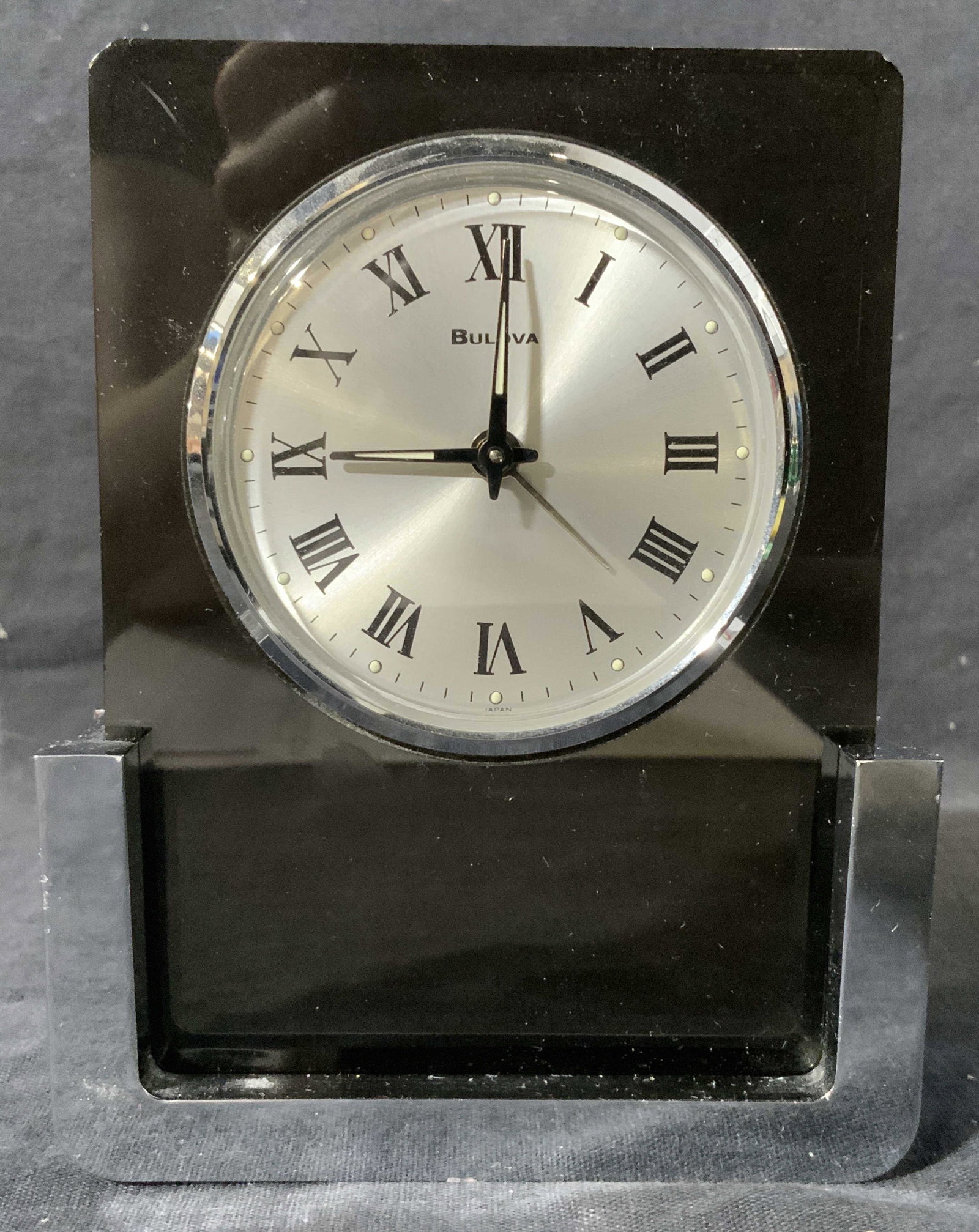BULOVA Tabletop Timepiece: BULOVA Tabletop Timepiece, clock face reads ‘BULOVA’, dark toned translucent body with silver toned metallic base, body removable from base, not tested for functionality, measures 4 x 5 x 1 1/2 in