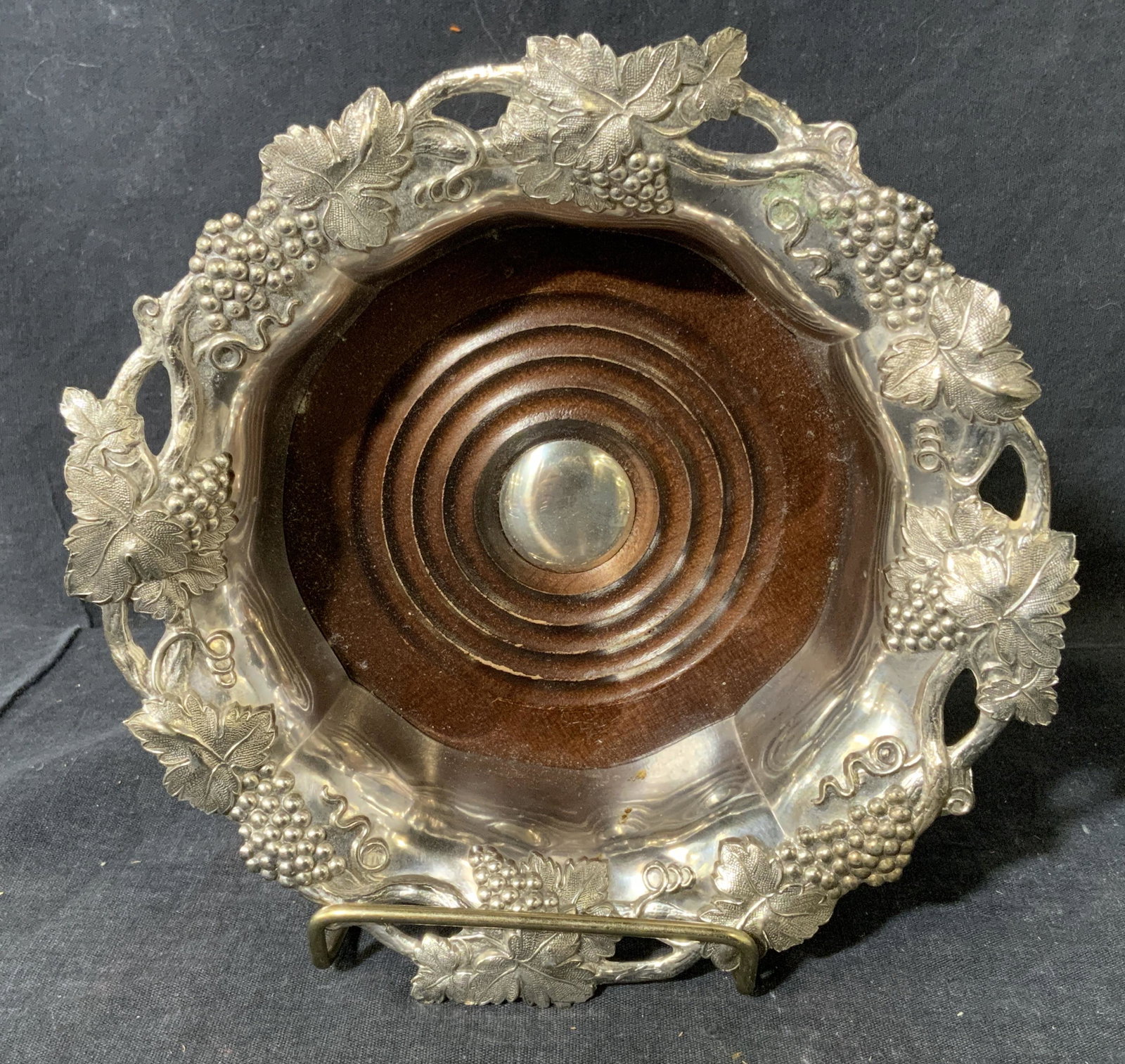 CORBELL SILVER Silver Plated Wine Bottle Coaster: Silver plated wine coaster, by CORNELL SILVER. Rim is cast to resemble grape vines, wooden well. Wear is consistent with age and use. Measures approx 2 inches h and 7 inches w. Wine accessories, decor