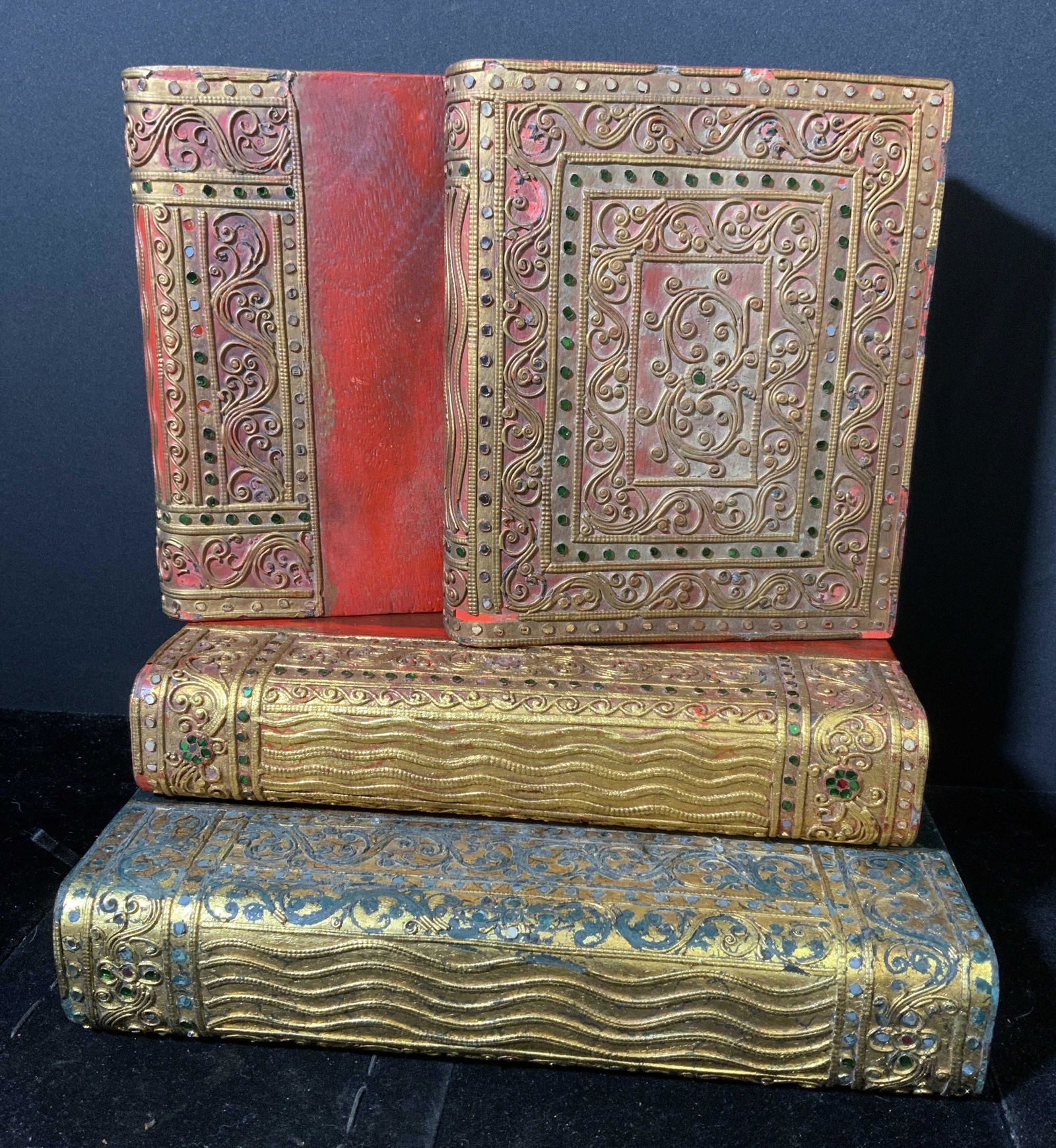 Lot 4 Carved Wooden Books w Inlaid Glass: Set 4 carved wooden books, appear to be vintage. Bindings are colored with gilt paint, decorated with inlaid colored glass. Wear is consistent with age and use, chipping to pieces, loss to inlaid glas