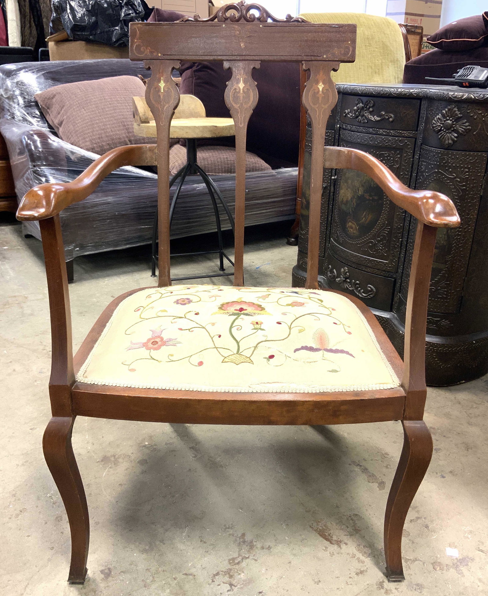 Vntg Low End Chair W Gimp Edged Seat Cushion: Chair is vintage possibly antique. Chair has carved wooden armrests. Piece has inlaid marquetry, parquetry detail. Chair has upholstered seat cushion with multi toned floral, vine and leaf embroidered