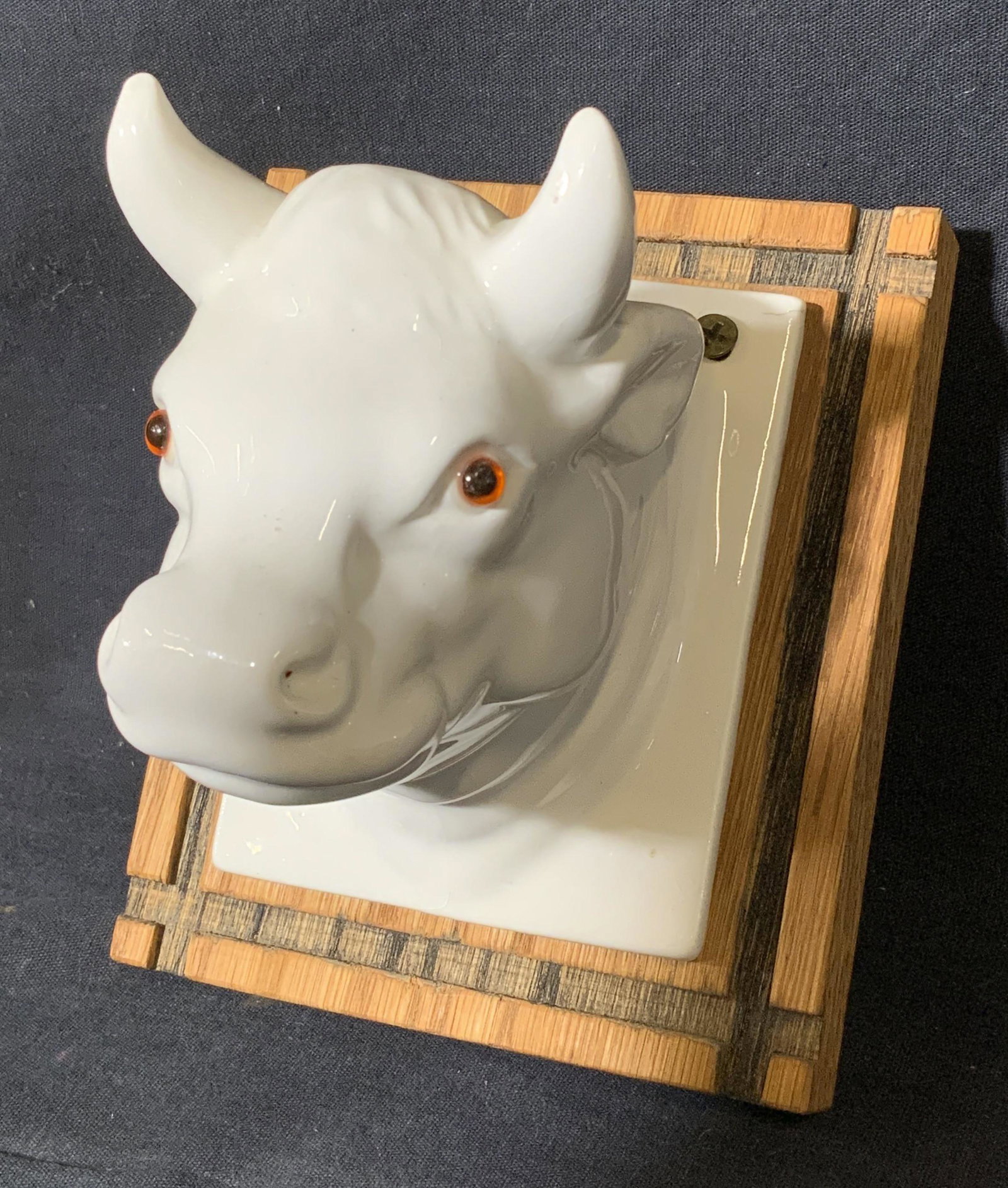 Mounted Ceramic Ox Head Figural Decor: Mounted Ceramic Ox Head, head made of ceramic with eyes possibly made from glass, mounted on wood tile, measures 4 5/8 l x 5 3/8 h inches, 4 3/8 inches deep, wear Consistent with age and use. Artwork,