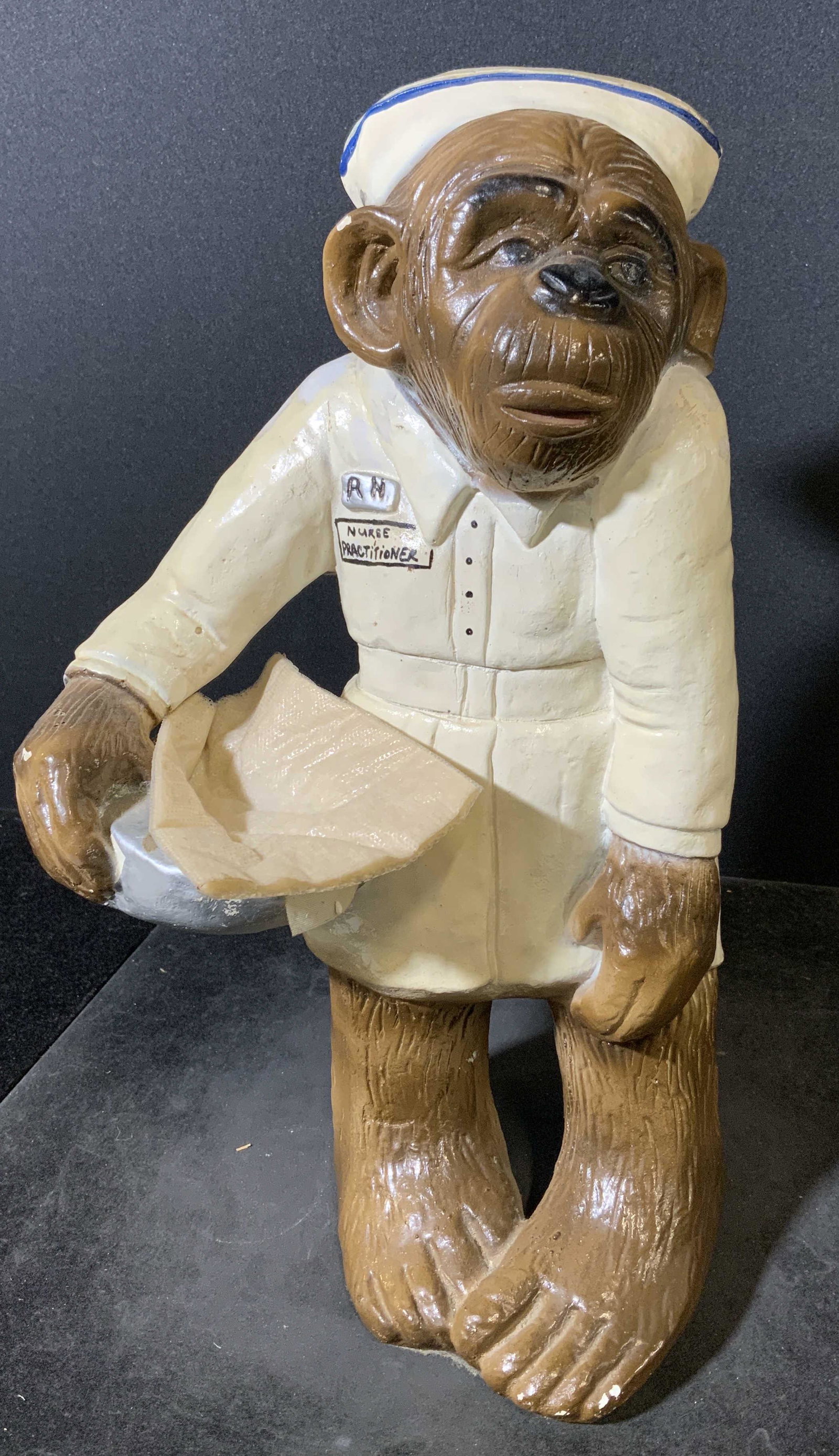 Vintage Hand Painted Ceramic Chimpanzee Nurse Fig: Hand painted ceramic figural. Depicts a chimp wearing a nurses uniform, front of jacket reads as RN NURSE PRACTITIONER, the.figure is holding a bed pan and towel. Wear is consistent with age and use, 