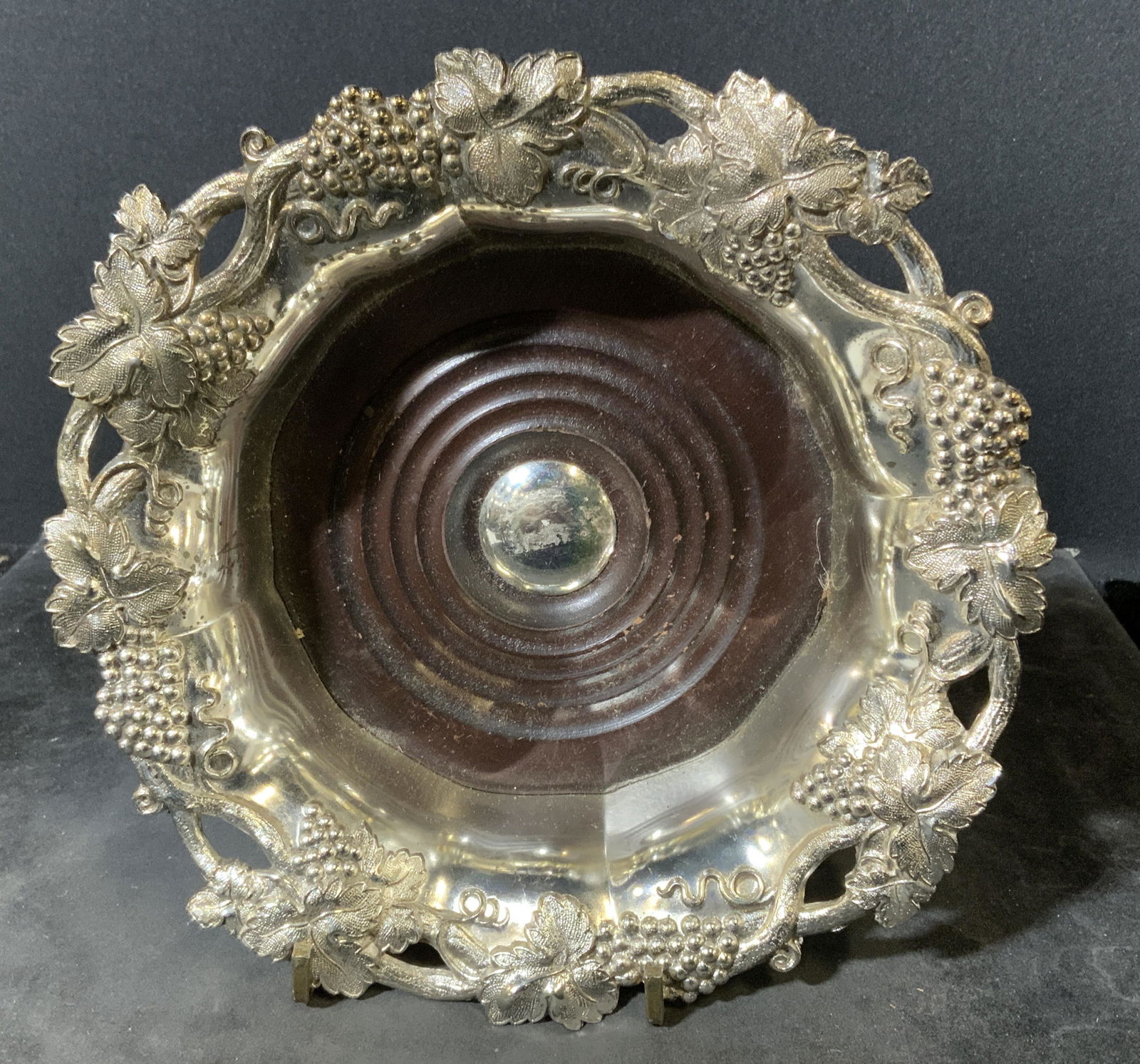 Vintage Cast Metal Wine Coaster: Metal and wood wine coaster, appears to be vintage. Cast grape and vine-like detailing decorate the rim. Center is wooden, decorated with carved concentric circles. Wear is consistent with age and use
