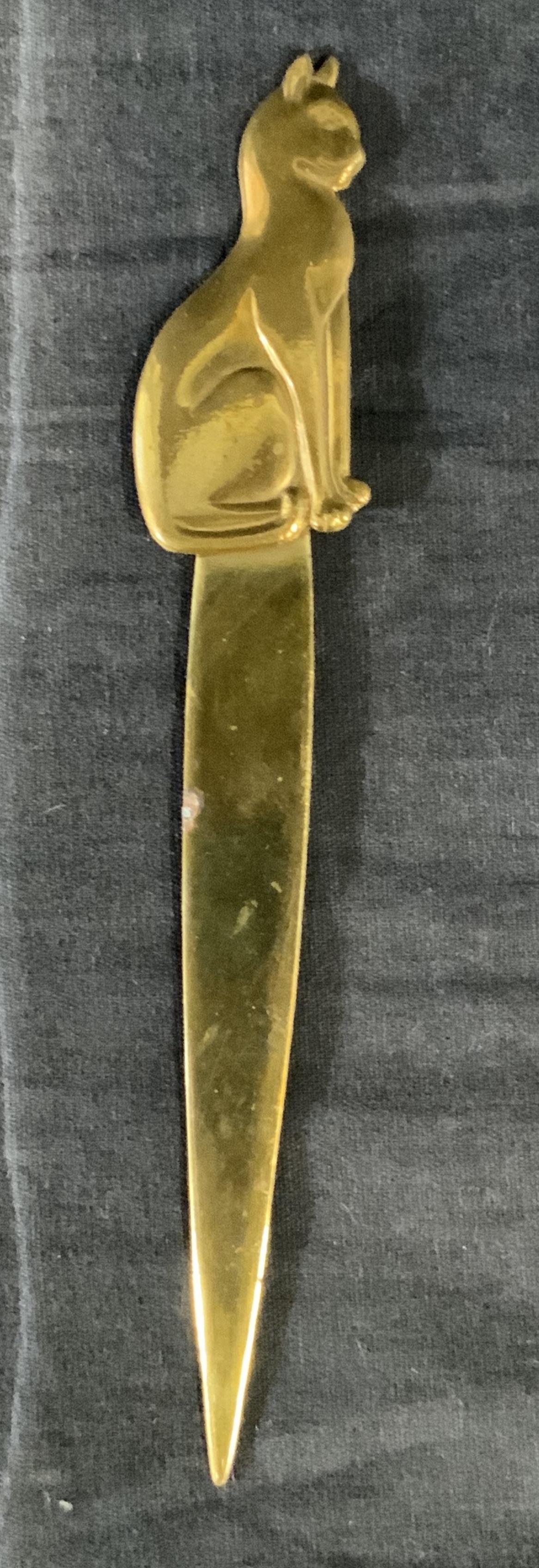 Brass Cat Letter Opener: Brass Letter opener with a figure of a sitting cat. Height is approximately 7in and width of cat is 1in, blade is less than an inch wide. Wear is consistent with use and age, areas of verdigris and so