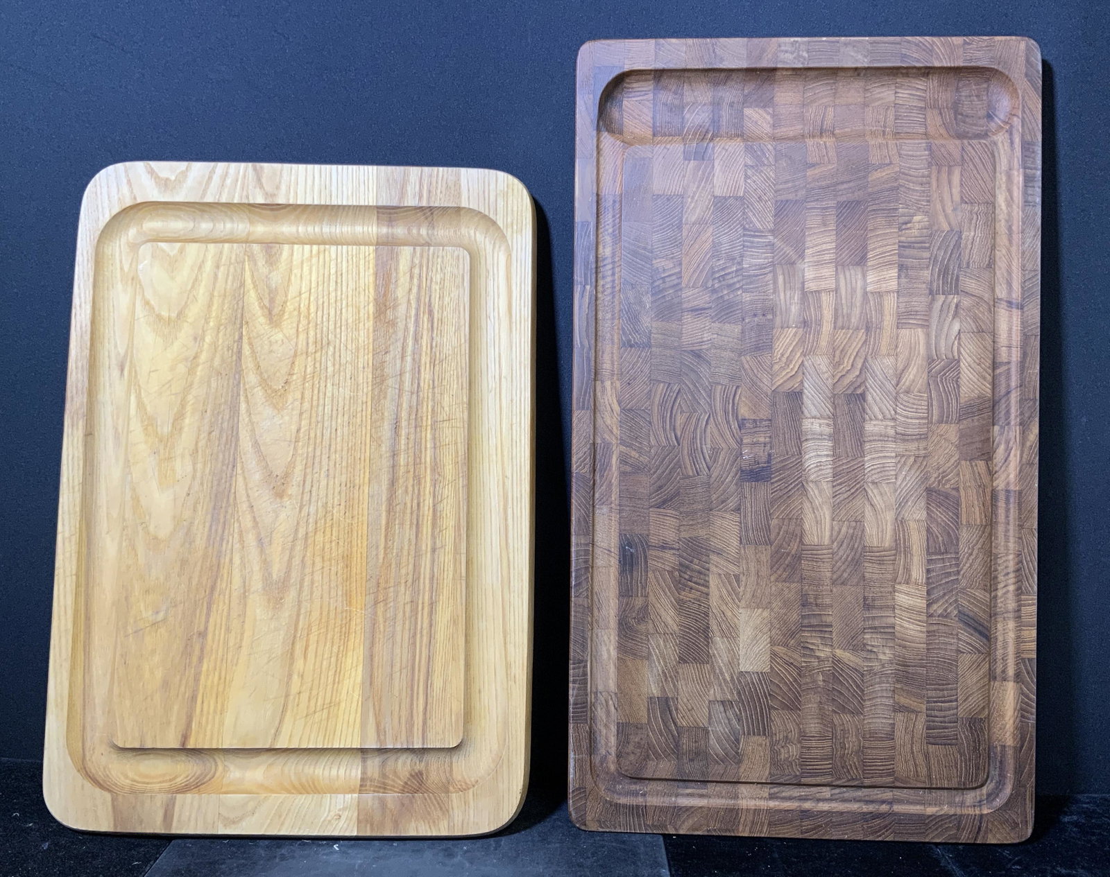 Lot 2 Hardwood Carving Boards: Lot 2 carving boards. Both crafted from wood, underside of one marked DANSK. Grooves carved into both boards. Wear is consistent with use. Largest board measures approx 23 inches long, 13.25 inches w.