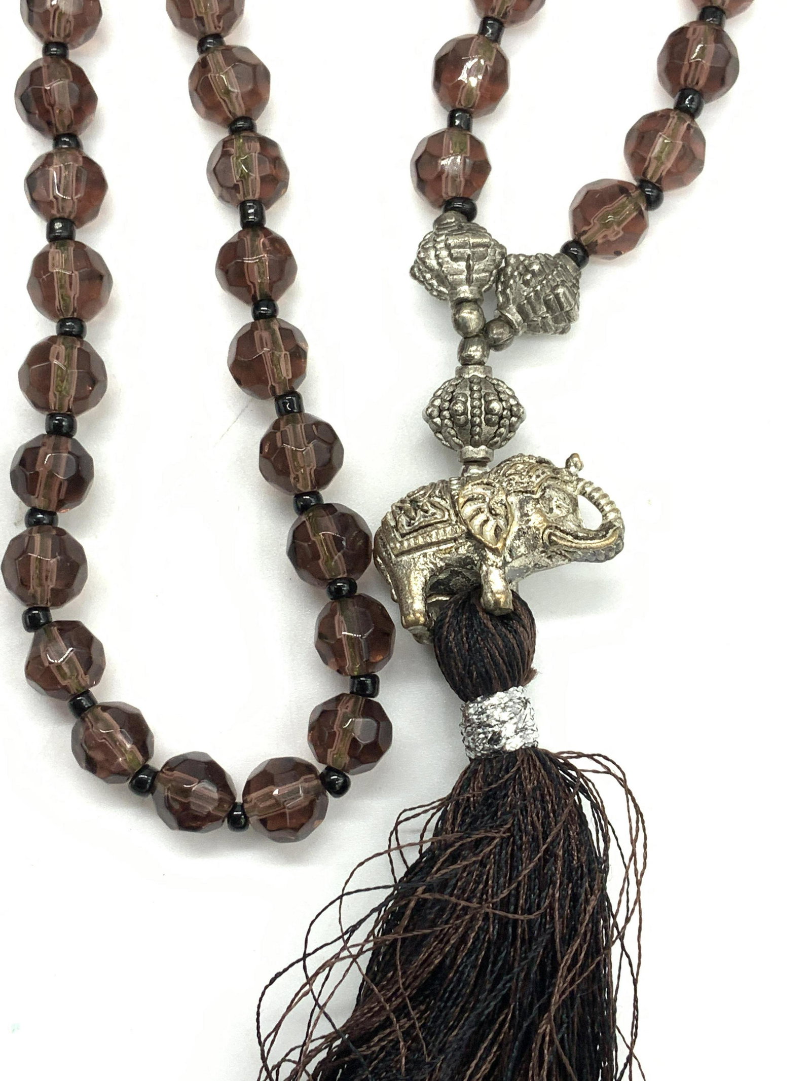 Glass Bead Tassel Necklace with Elephant Bail: Asian Style Glass Bead necklace, accented with elephant figural that lead to a fun tassel. Beads are the color of Smokey Quartz with a hint of purple. Tassel 5 in. Long, Necklace 28 in. Long. Asian el