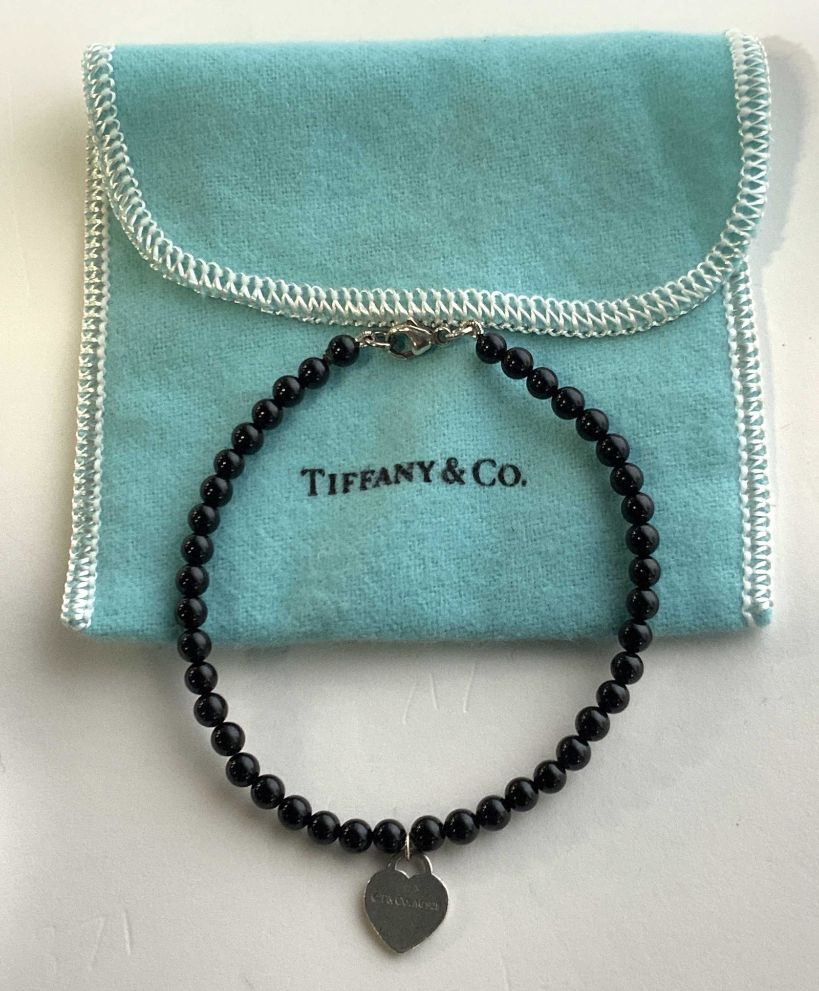 TIFFANY & Co. Sterling Silver Heart Bracelet: A Tiffany & Co. bracelet with black natural gem stone beads, Sterling silver clasps and heart charm. Comes in original Tiffany & Co. dust bag. Trademarked on heart charm ‘c. T&Co. AG 925’ and ‘P