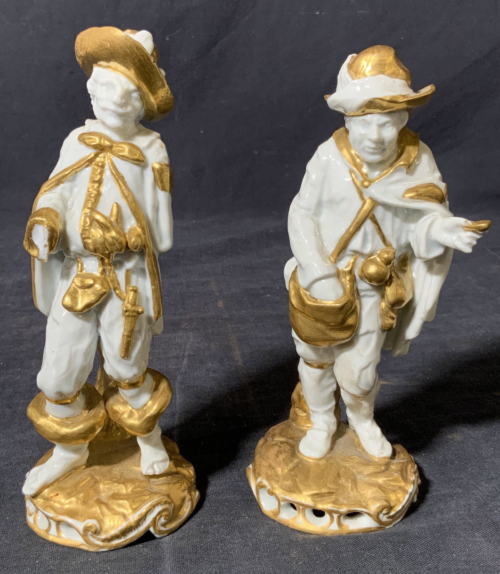 Vintage Capodimonte Porcelain 2 Male Figurals: A set of 2 Vintage male Figures trademarked Capodimonte Porcelain on undersides, with gold gilt accents throughout white figures, featuring men of medieval dress each with distinct stances and gesture