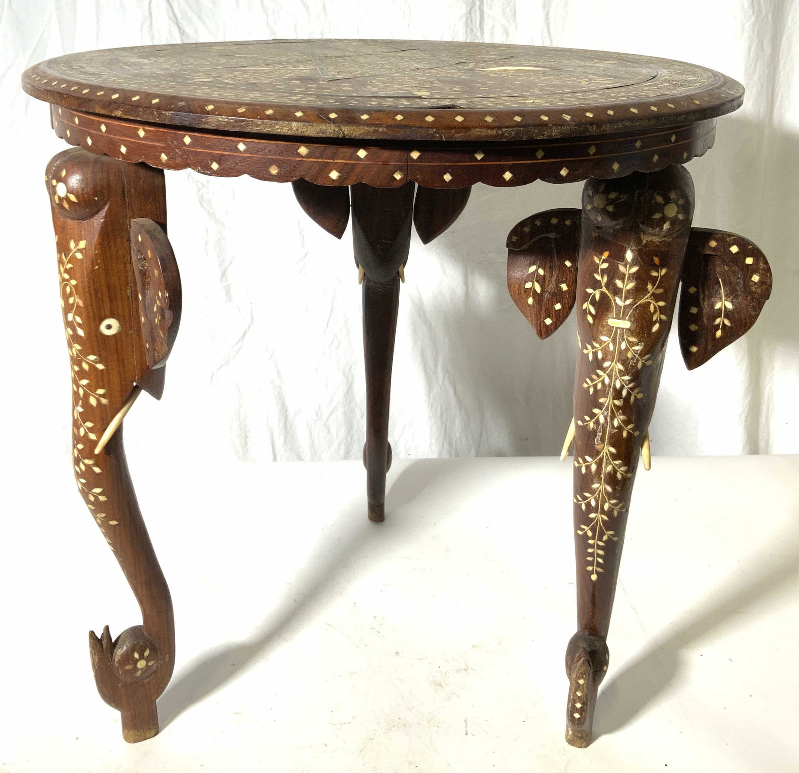 Indian Inlaid Bone Marquetry Elephant Leg Table: Side table is wooden with intricate inlaid bone detail. Piece has 3 legs each with elephant style structures including ears, eyes & tusk shapes. Table has circular shaped top. Piece has intricate inla