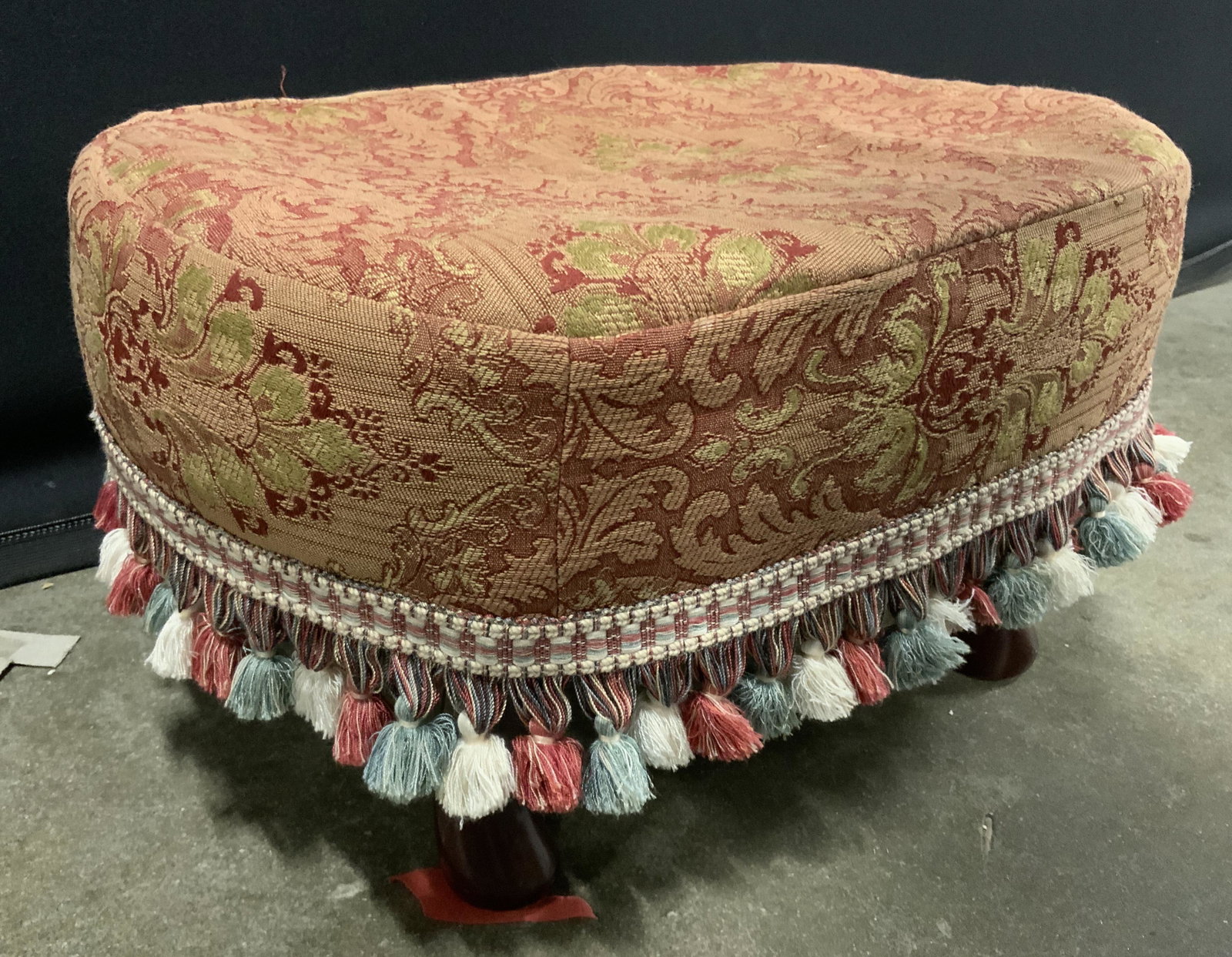 COASTER CO OF AMERICA Slip Cover Foot Stool: Underside of foot stool has tag which reads COASTER CO OF AMERICA. Foot stool has slip cover with gimp & tasseled edges. Footstool has 4 carved wooden feet. Piece has red green & gold toned slip cover