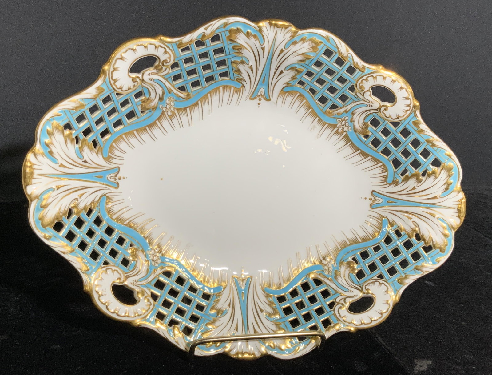 Vintage MINTONS Signed English Porcelain Plate: A vintage white hued porcelain plate with pierced porcelain edges and gilt line work. Blue hued designs throughout. Measures approx 1.5H x 10.5W in. Measured at widest point. Underside reads MINTONS, 