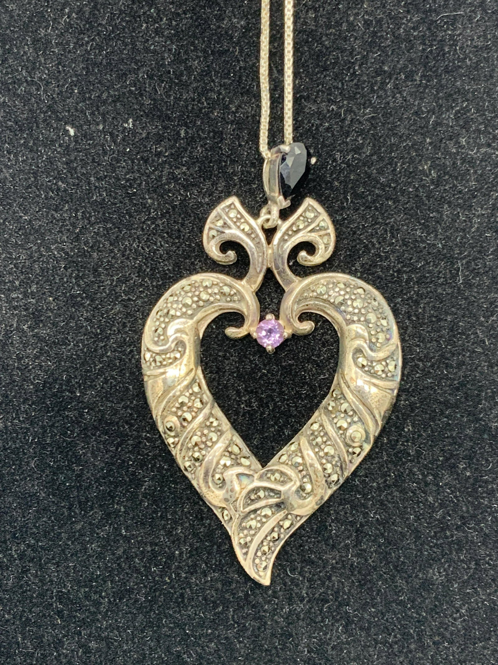 Sterling Silver Heart Pendant Necklace: A sterling silver necklace with a heart pendant bejeweled with Marcasite and has a glass purple crystal and black glass crystal accents. Pendant and chain are marked 925. Chain is approximately 15.5 i