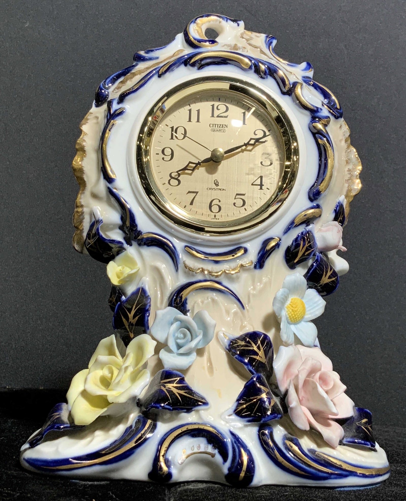 Vntg CITIZEN CRYSTRON Porcelain Mantel Clock: Clock face reads CITIZEN CRYSTRON. Piece is white toned with ornate blue and gold toned detail in addition to multi toned floral detail. Clock face is gold toned with black hands and numbers. Piece me