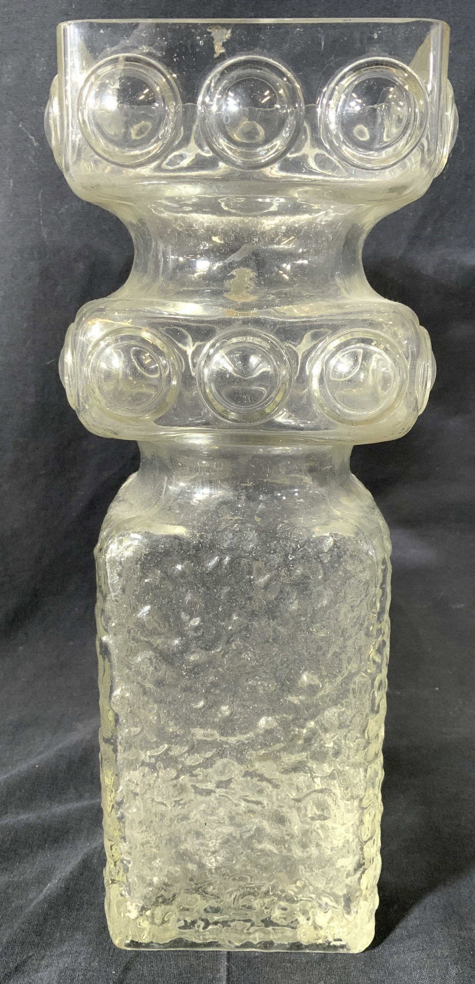 Vintage Glass Vase Centerpiece Decor: Vase is glass. Piece has beveled circular detail near top. Lower half of piece has textured detail. Neck of vase has double tapered structure. Mouth of vase has square shape with rounded corners. Piec