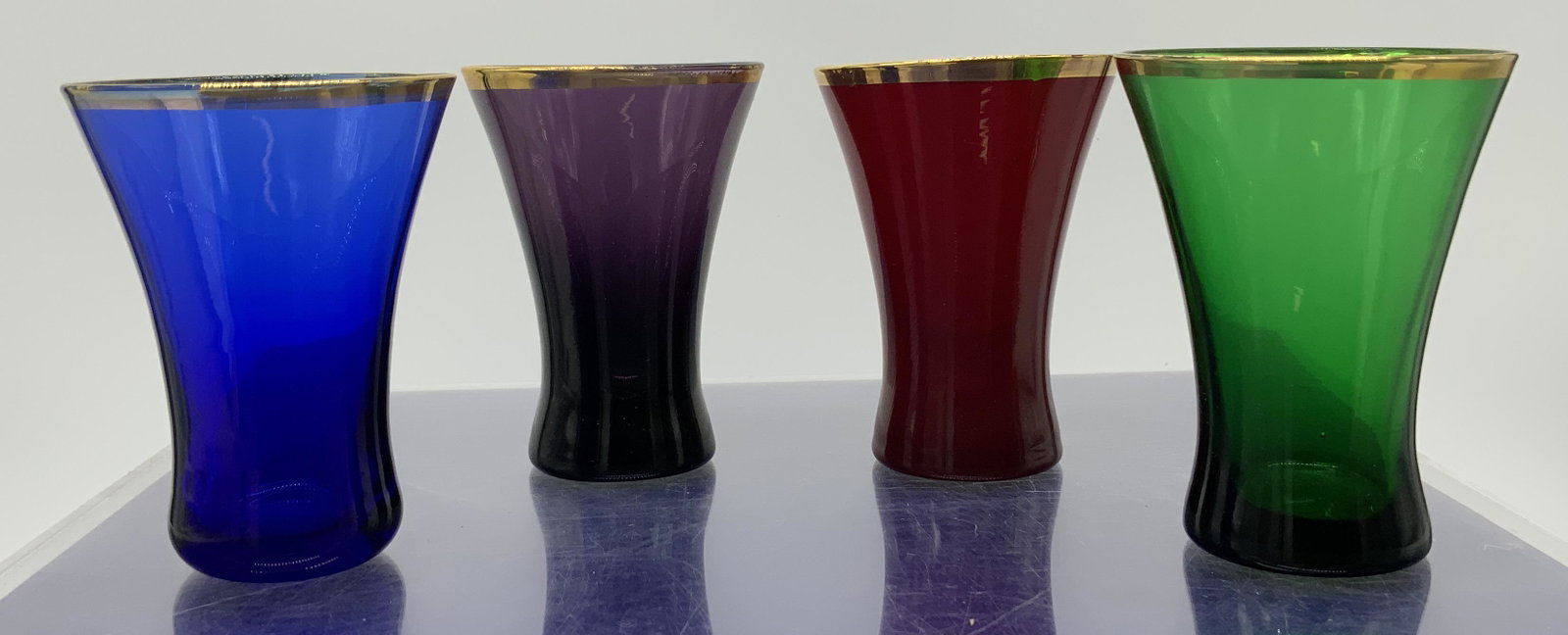Lot 4 Multicolor Glass Shooter Glasses: Lot 4 Multicolor Glass Shooter Glasses, no apparent inscriptions or mark to piece, subject four differently colored shooter glasses with gold toned gilt rims, measure 3 x 2 1/4 x 2 1/4 inches, surface