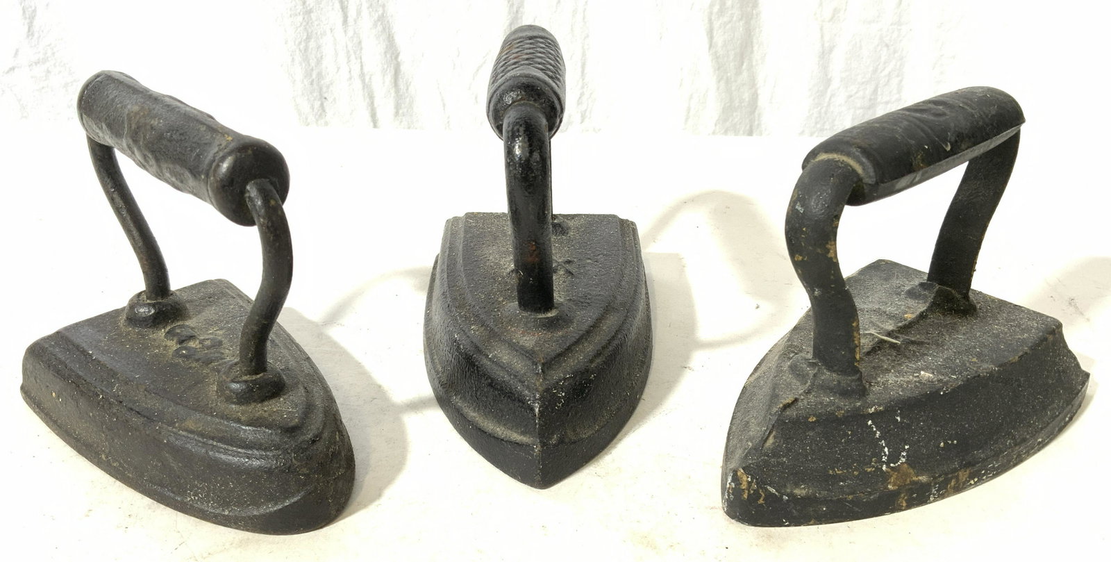 Lot 3 Black Antique Irons: Lot includes 3 irons. Each are black toned. Irons are significantly weighted. Each piece has slightly differing structures. Largest iron measures 6 inches long 3.5 inches wide 5 tall. Irons, antique i