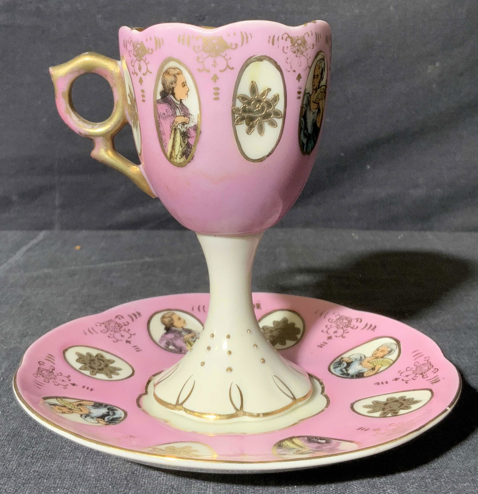 Porcelain Stemmed Glass with Saucer: Porcelain Stemmed Glass with Saucer, marking to underside reads ‘6165 C’, subject a stemmed and handled cup with matching saucer, pink toned base with French style portrait details, saucer measure