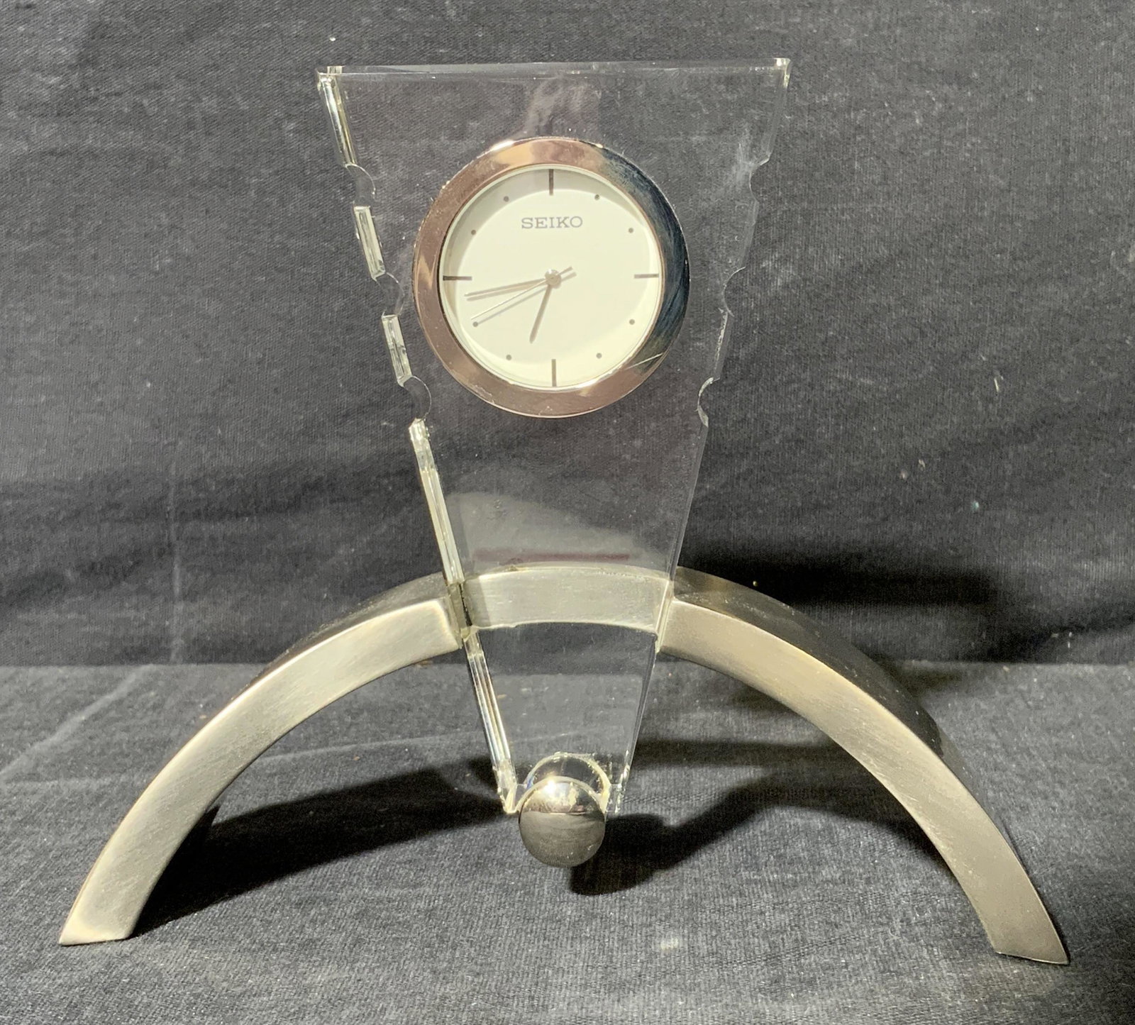SEIKO Tabletop Clock: SEIKO Tabletop Clock GHQ008S, marking to clock face reads ‘SEIKO’, subject a clock face set into a clear triangular form held in a metallic arch, measures 4 1/2 x 5 1/4 x 1 3/4 inches, surface wea