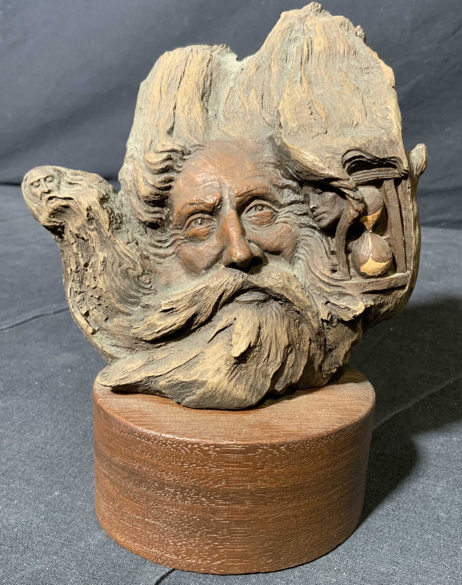 Signed CAIN Carved Composite Male Face Figure: Backside of piece is signed CAIN. Piece is brown toned and depicts a large male face figure, small male face figure and hour glass. Piece appears to be composite possibly wooden. Base is oval shaped. 