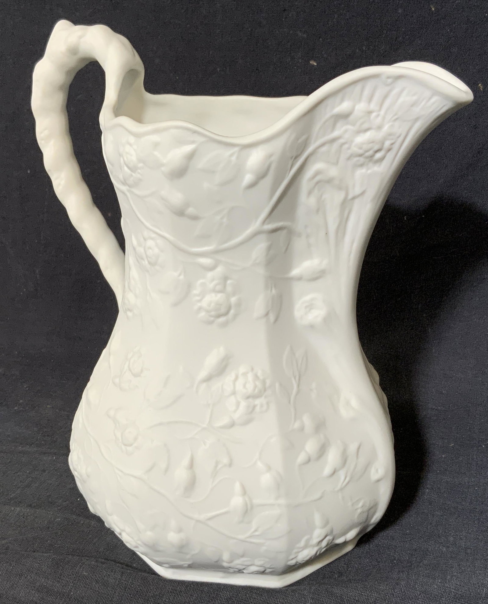 Bisque Porcelain Pitcher: Bisque Porcelain pitcher. Decorated with cast flowering vine detail, in relief. Underside reads as â€˜Made in Mexicoâ€™. Measures approx 8.75 inches h and 8 inches w. Biscuit porcelain, bisqu